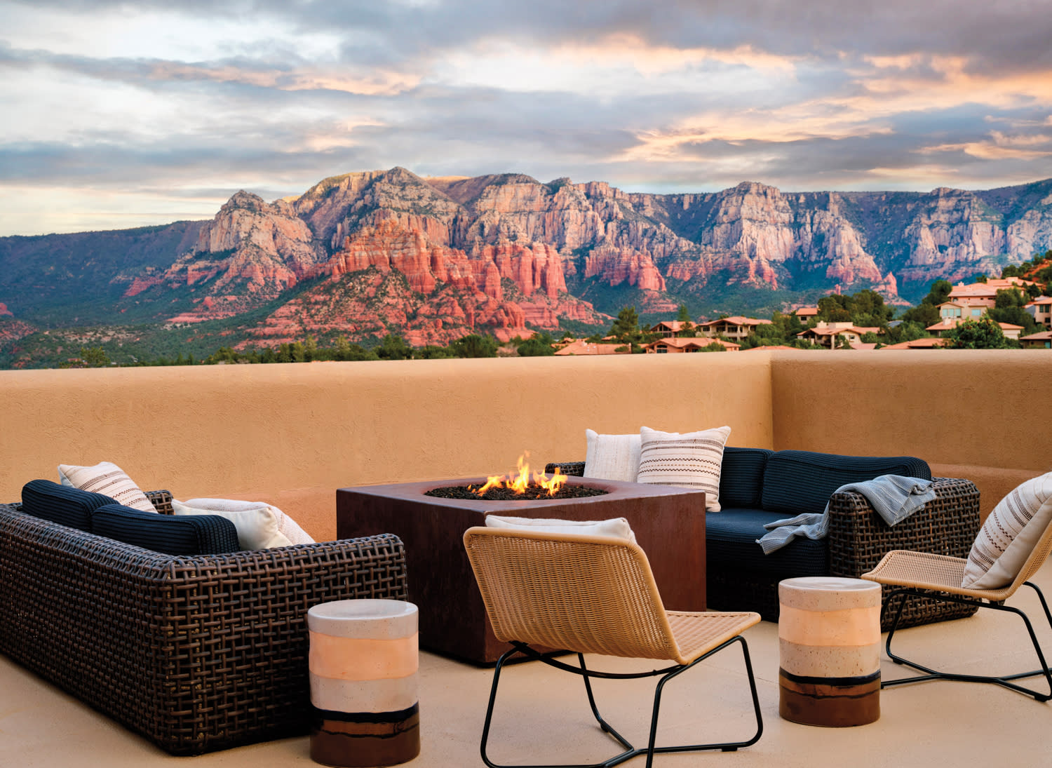 Rooftop sitting area with plush chairs and sofas around a fire pit with views of red mountains.