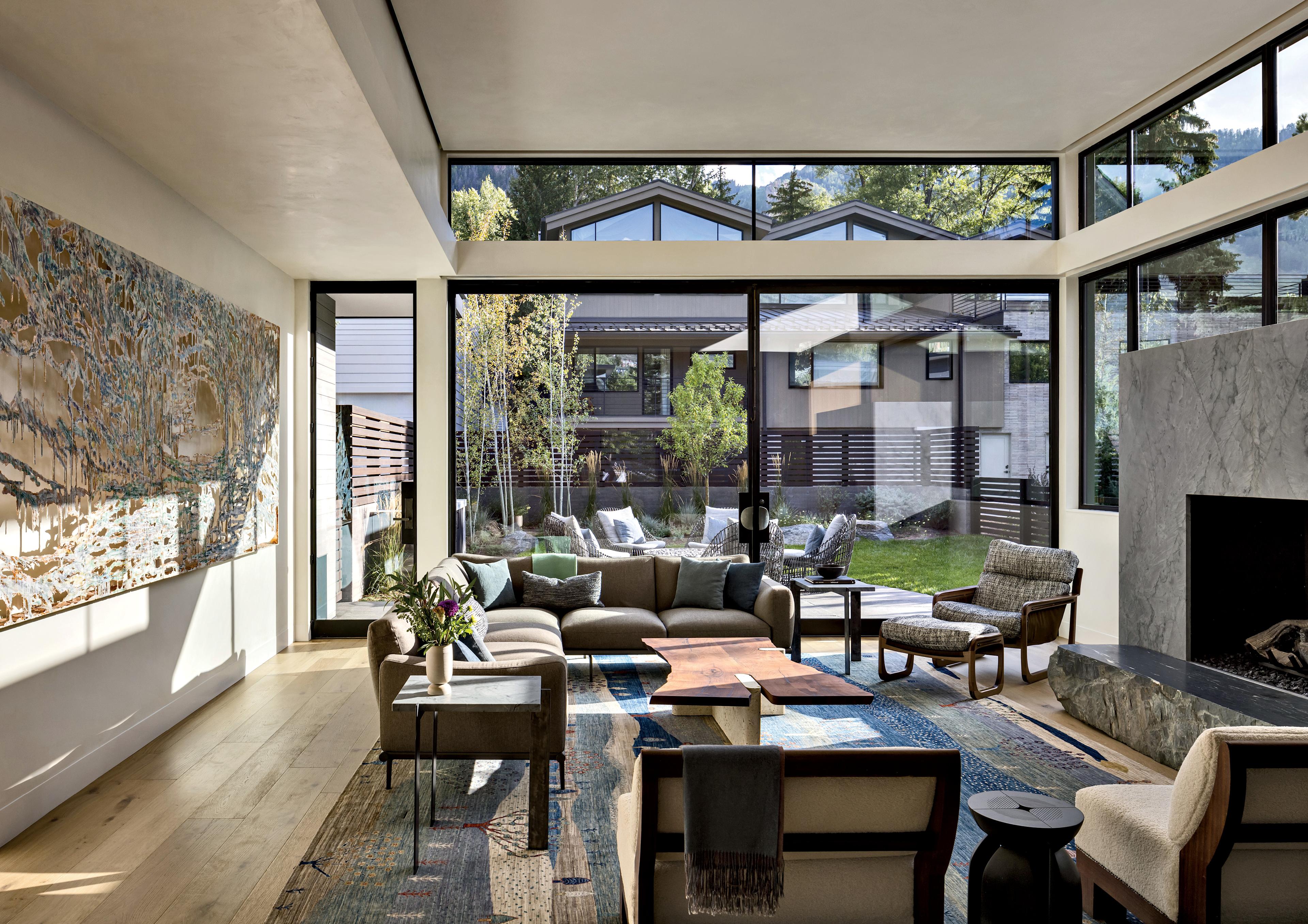 A sectional, lounge chair, ottoman, slipper chairs and coffee table sit near tall glass windows.