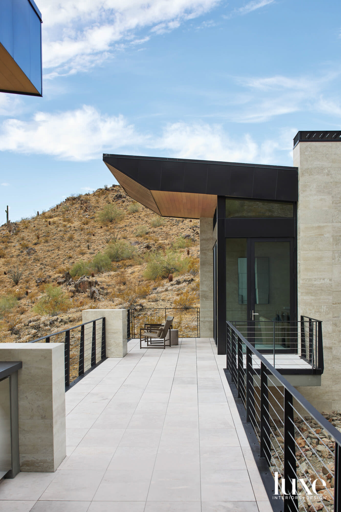 A deck on a modern home that is set against a mountain.