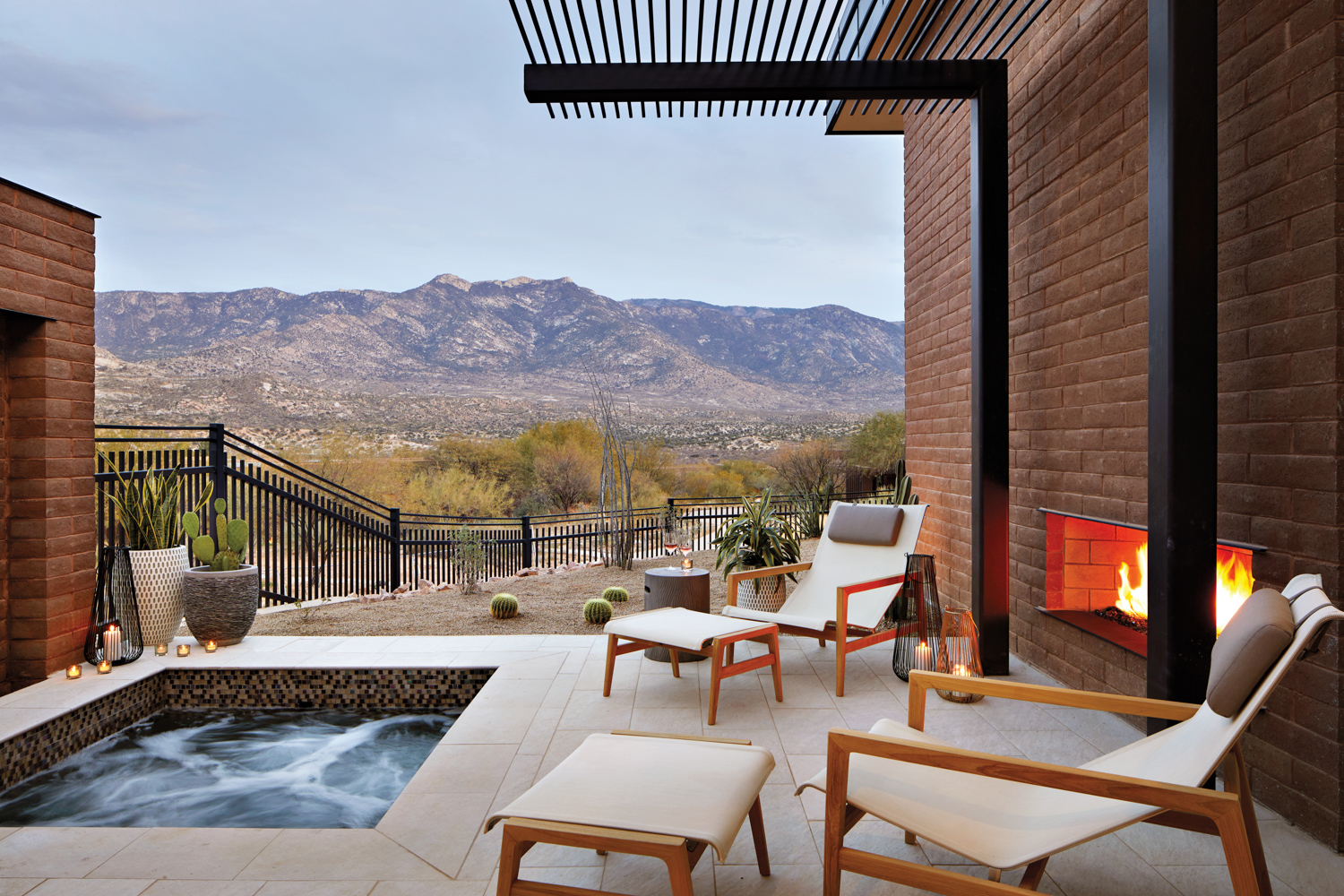 Patio space with hot tub, lounge chairs and a fireplace overlooking desert mountains.