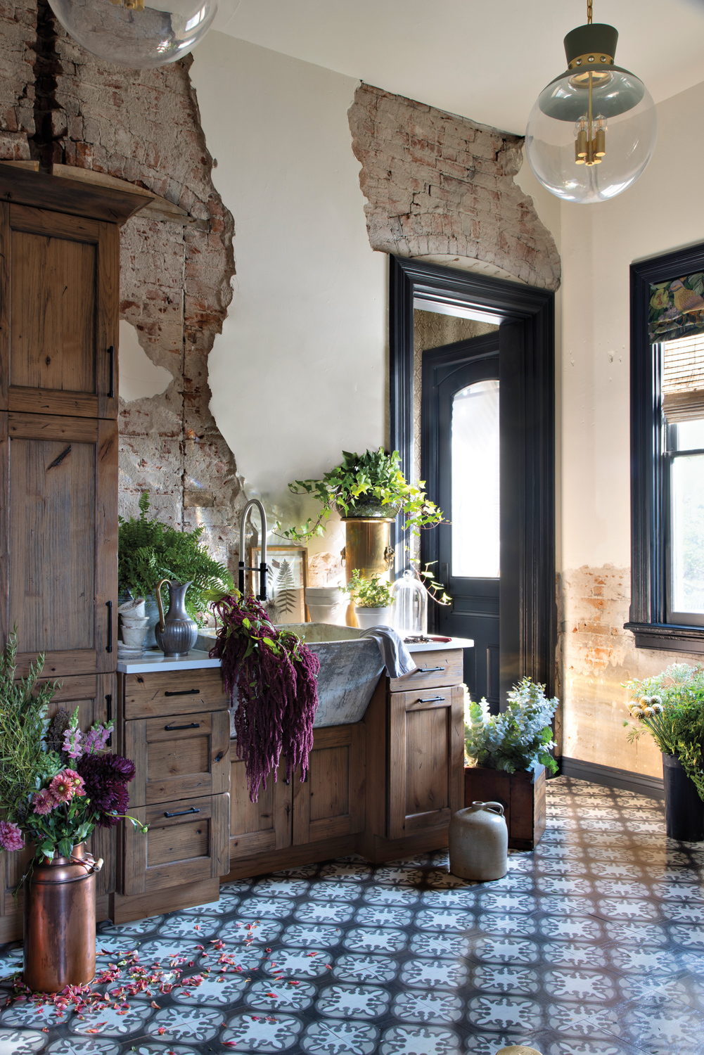 A garden room with portions of original old brick arch walls exposed and an apron-front sink filled with flowers.