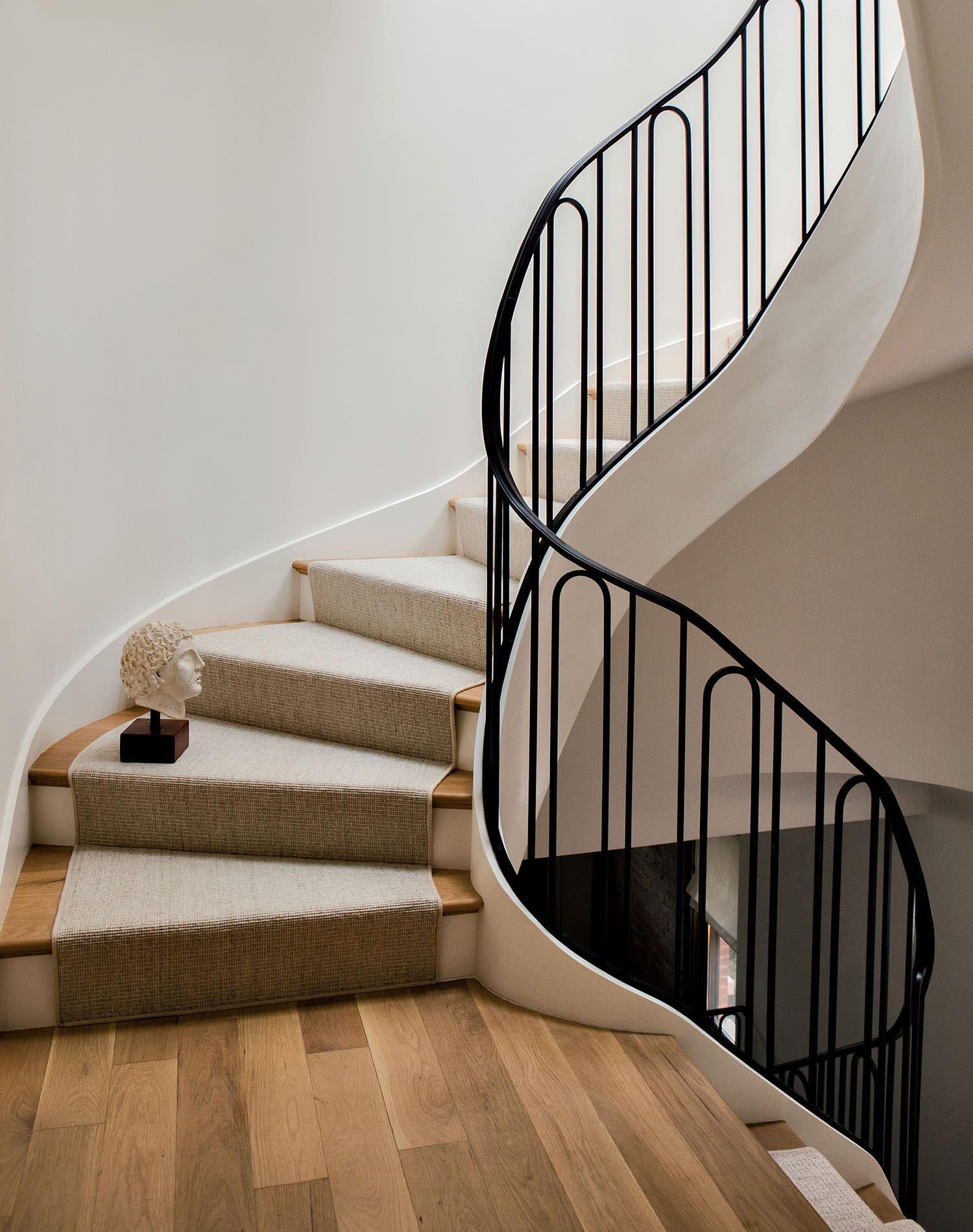 A curved staircase with a wrought-iron railing and a pale carpeted runner on the wood steps.
