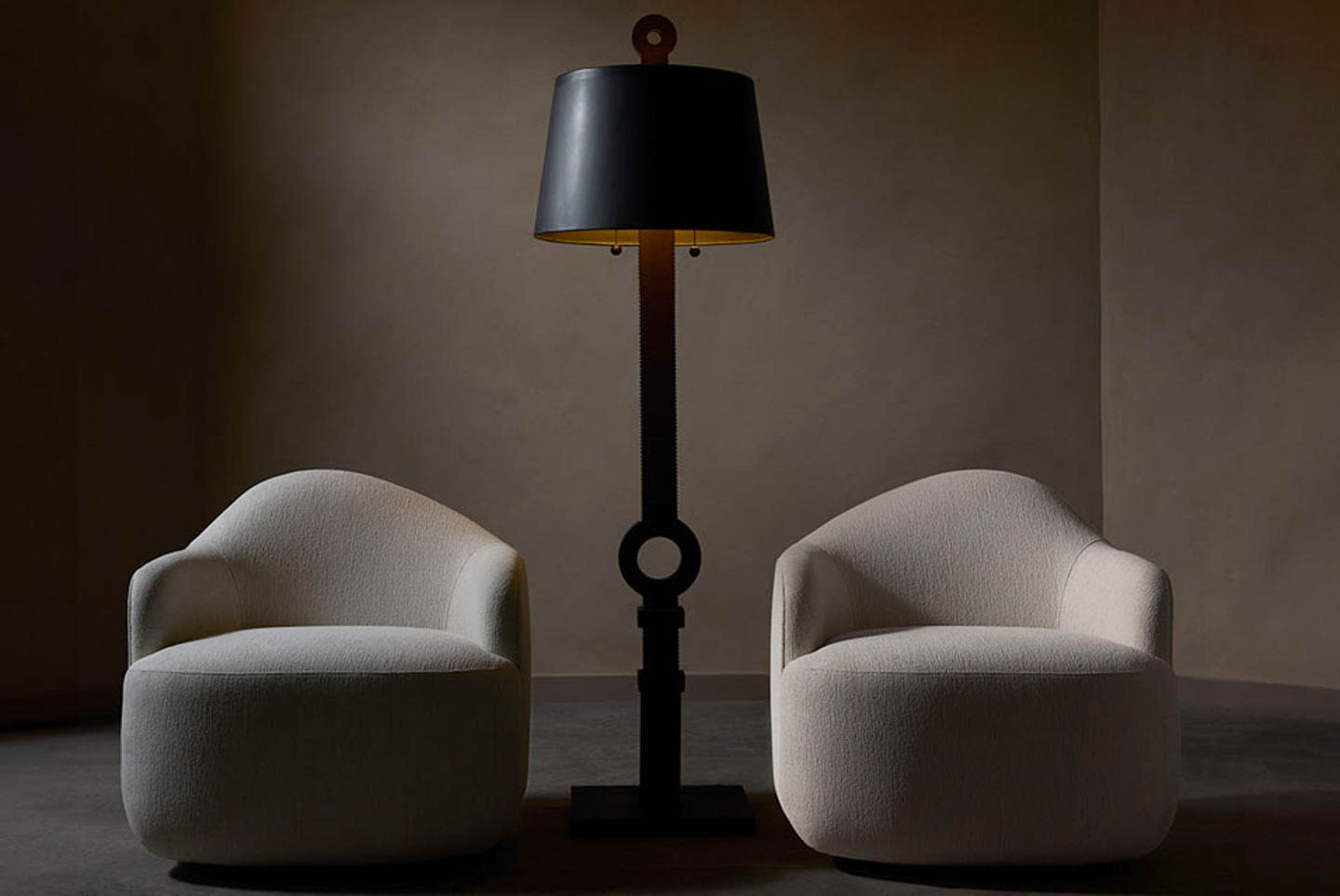 Two curved, cream armchairs flank a central tall black floor lamp in a softly lit room. The scene conveys a minimalist and elegant ambiance.