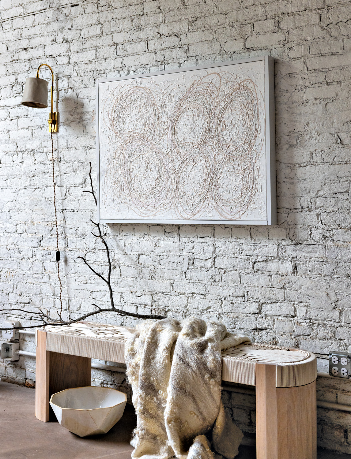 Abstract white artwork against a white brick wall and above a wood bench