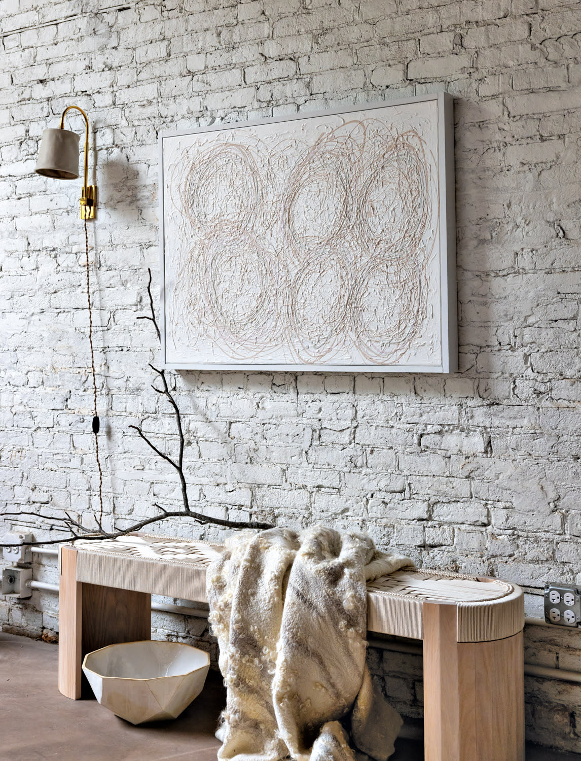 Abstract white artwork against a white brick wall and above a wood bench.