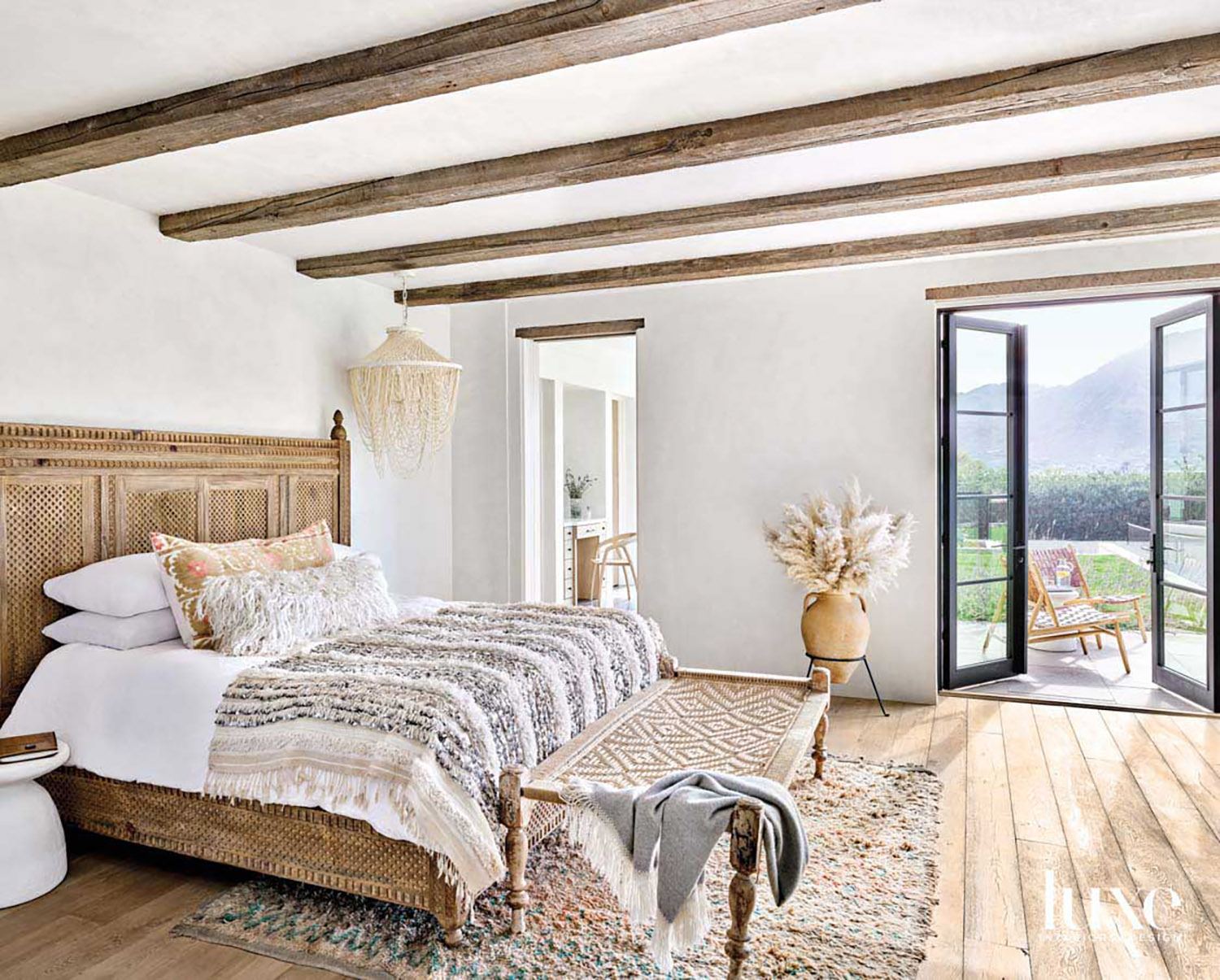 A carved wooden bed has textured linens and the ceiling in the zen bedroom has natural wood beams.