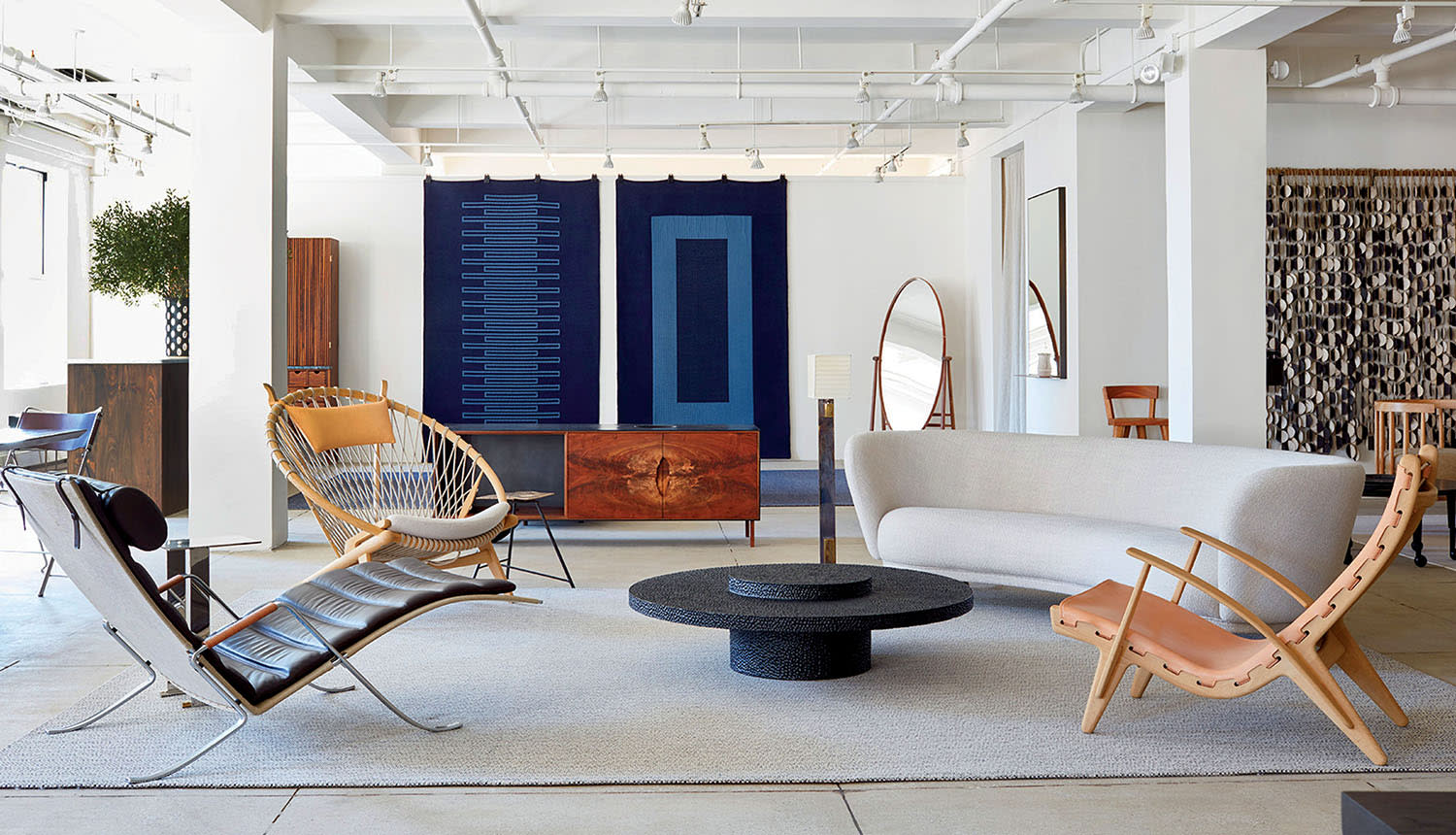 A crescent-shaped couch sits in a showroom with other seating, a mirror and tapestries.