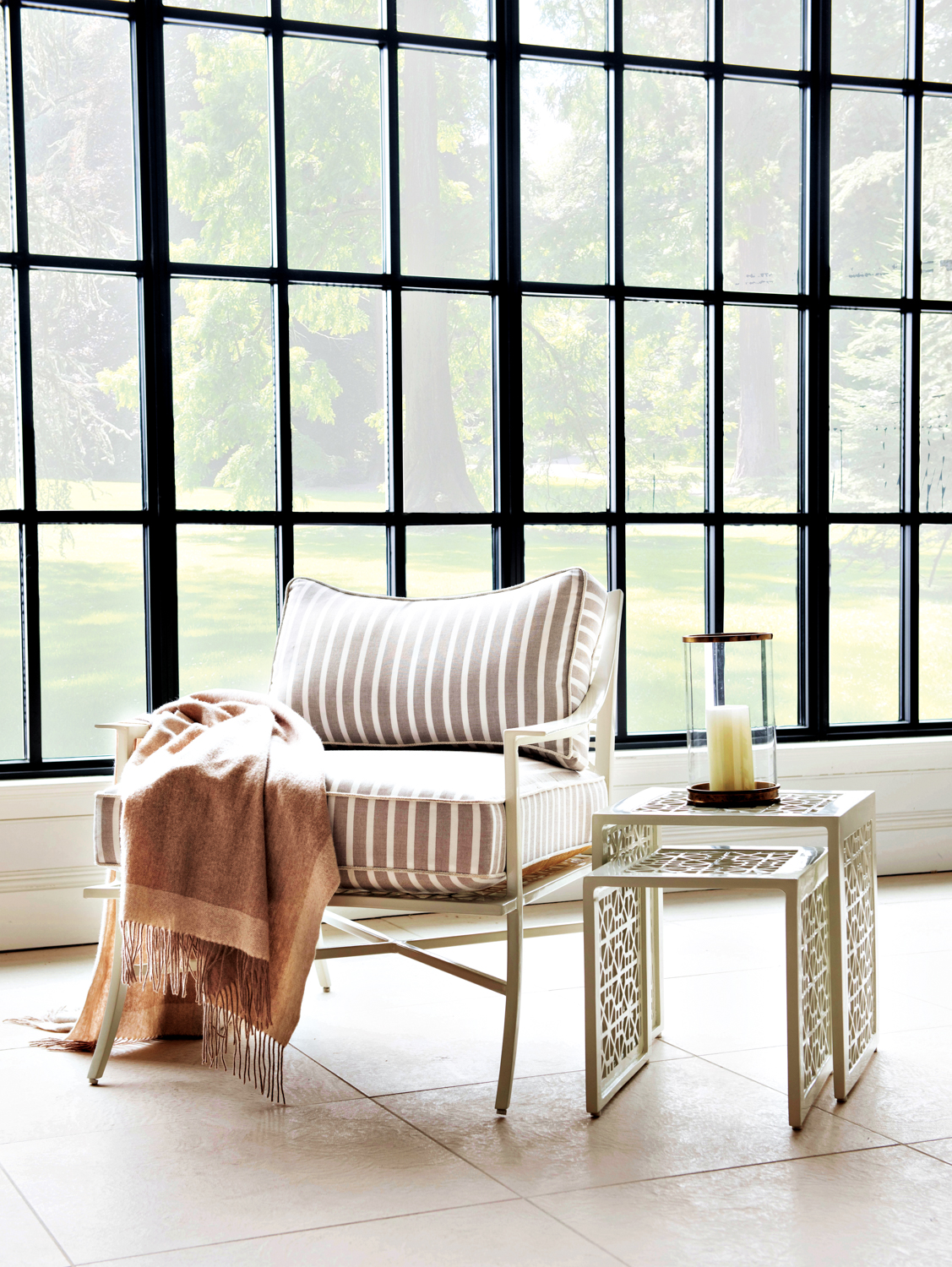 Outdoor armchair with striped cushions and nesting side tables in a windowed all seasons-type room