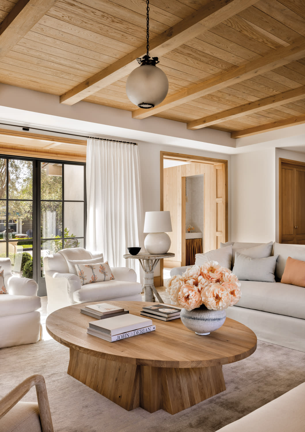 living room with round coffee table, white armchairs, couch, and a round side table topped with a table lamp in home by Marie Carson