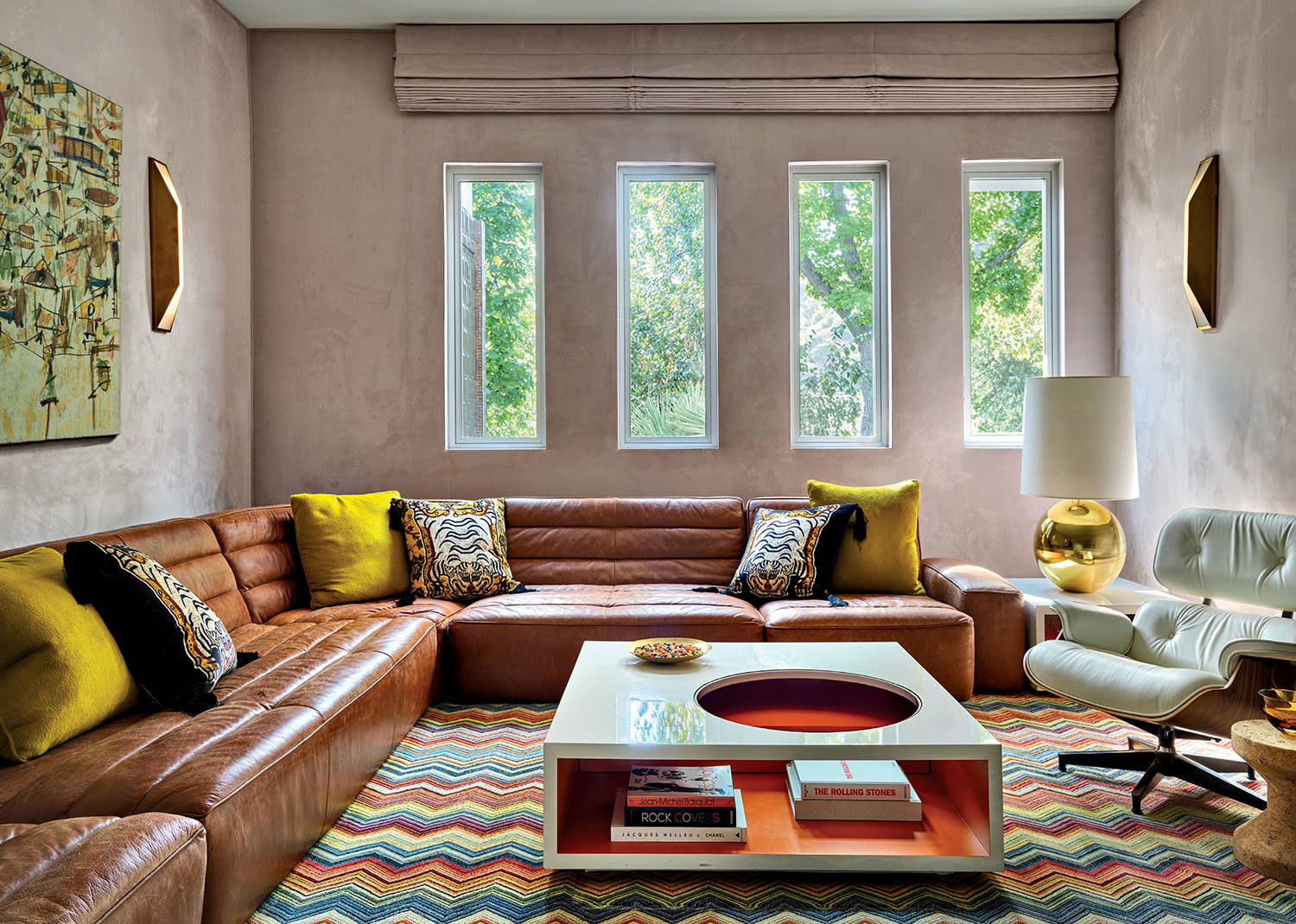 A media room with light-colored suede walls, a wraparound leather couch, modern coffee table and leather armchair.