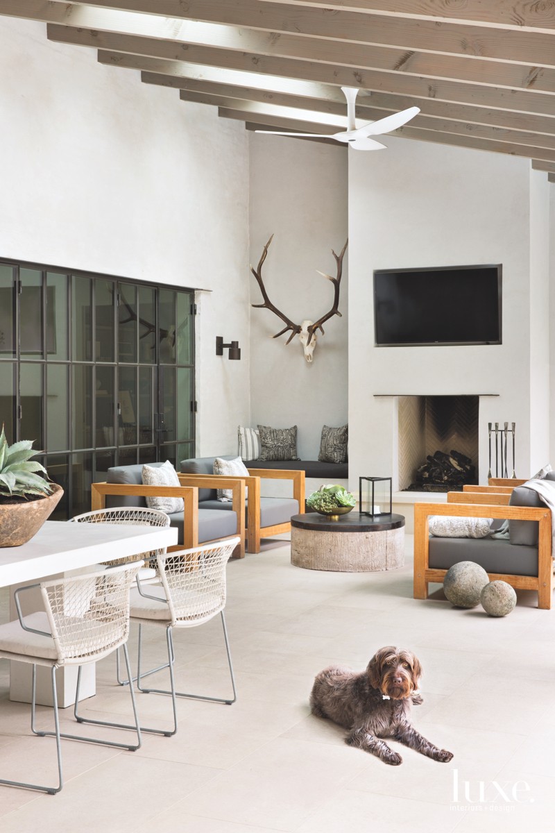 n the back patio of the home, constructed by builder Ben Bailey, chairs by Teak Warehouse with Sunbrella fabric-covered cushions and Kelly Wearstler throw pillows welcome conversation around a stucco fireplace. Texas Lightsmith crafted brass sconces designed by Seiders that frame the door. Metal-base dining chairs, also by Teak Warehouse, surround a cast-concrete dining table