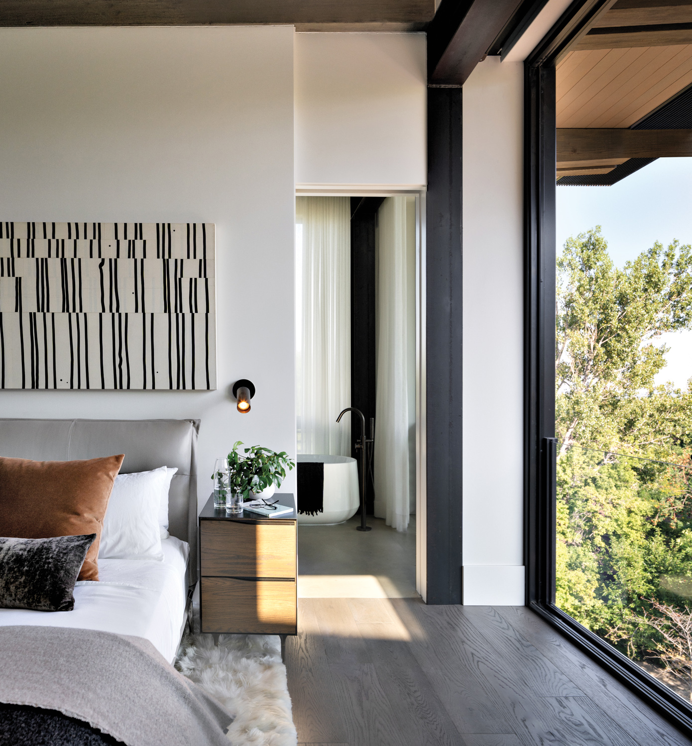 bedroom suite with a grey headboard with abstract artwork above it, wooden night stand and white rug