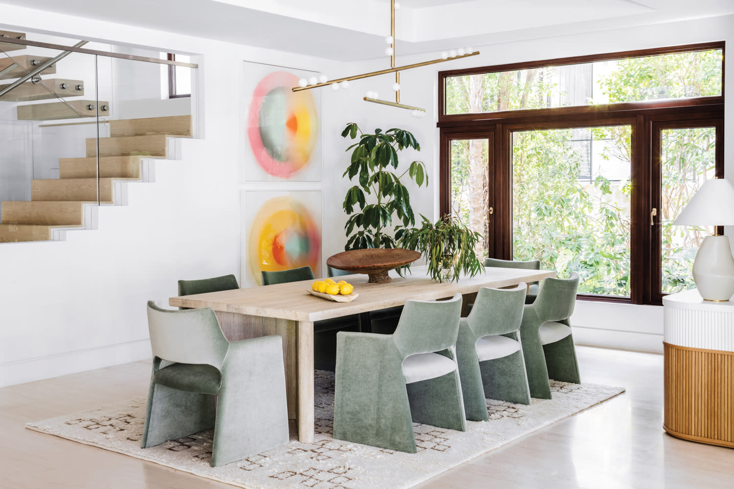 dining room with green velvet chairs, rectangular light wood table, circular artwork and gold bar light fixture