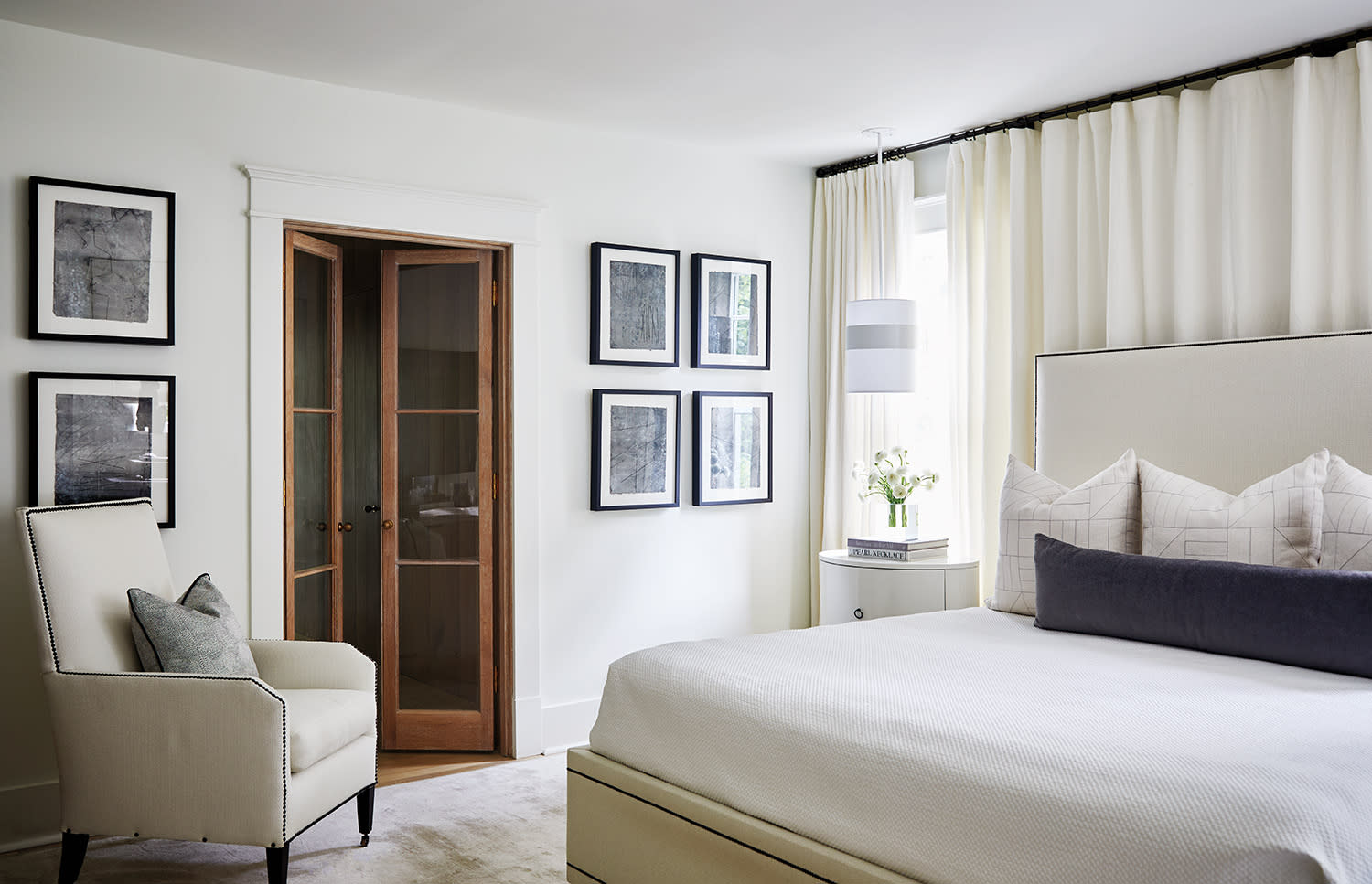 Serene bedroom with upholstered bed, framed art grid, and glass-paneled wooden doors.
