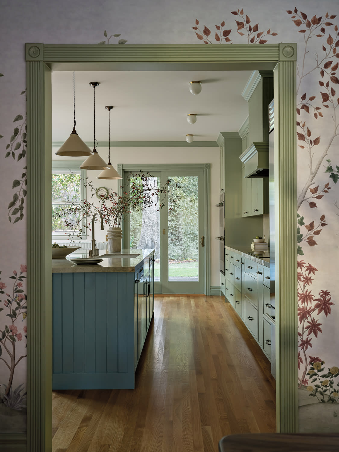 floral wallpaper outlines a green-trimmed doorway looking into a cozy kitchen