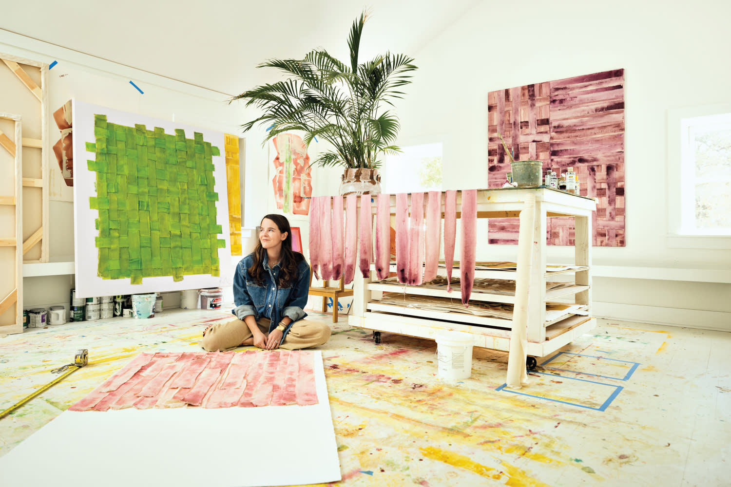 Laura Deems gently smiling within her studio surrounded by colorful artwork