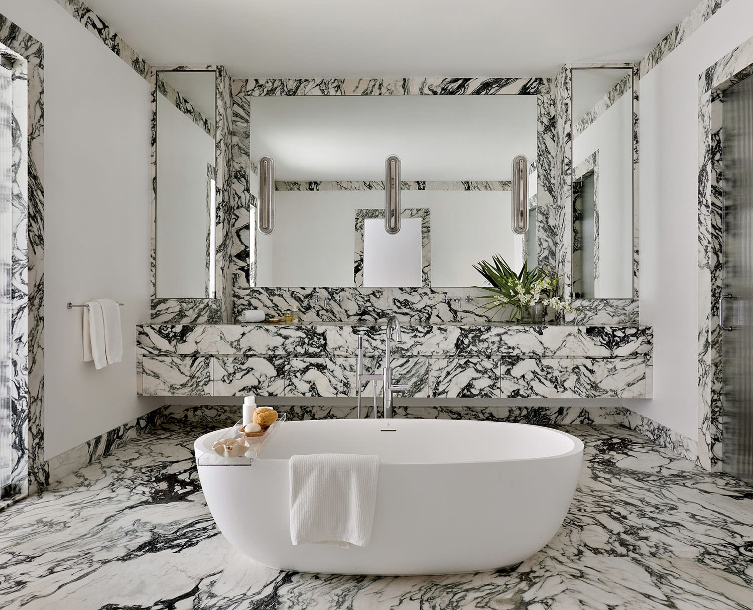 Luxurious bathroom with a centerpiece oval tub, surrounded by elegant black and white marble, featuring large mirrors and modern lighting.