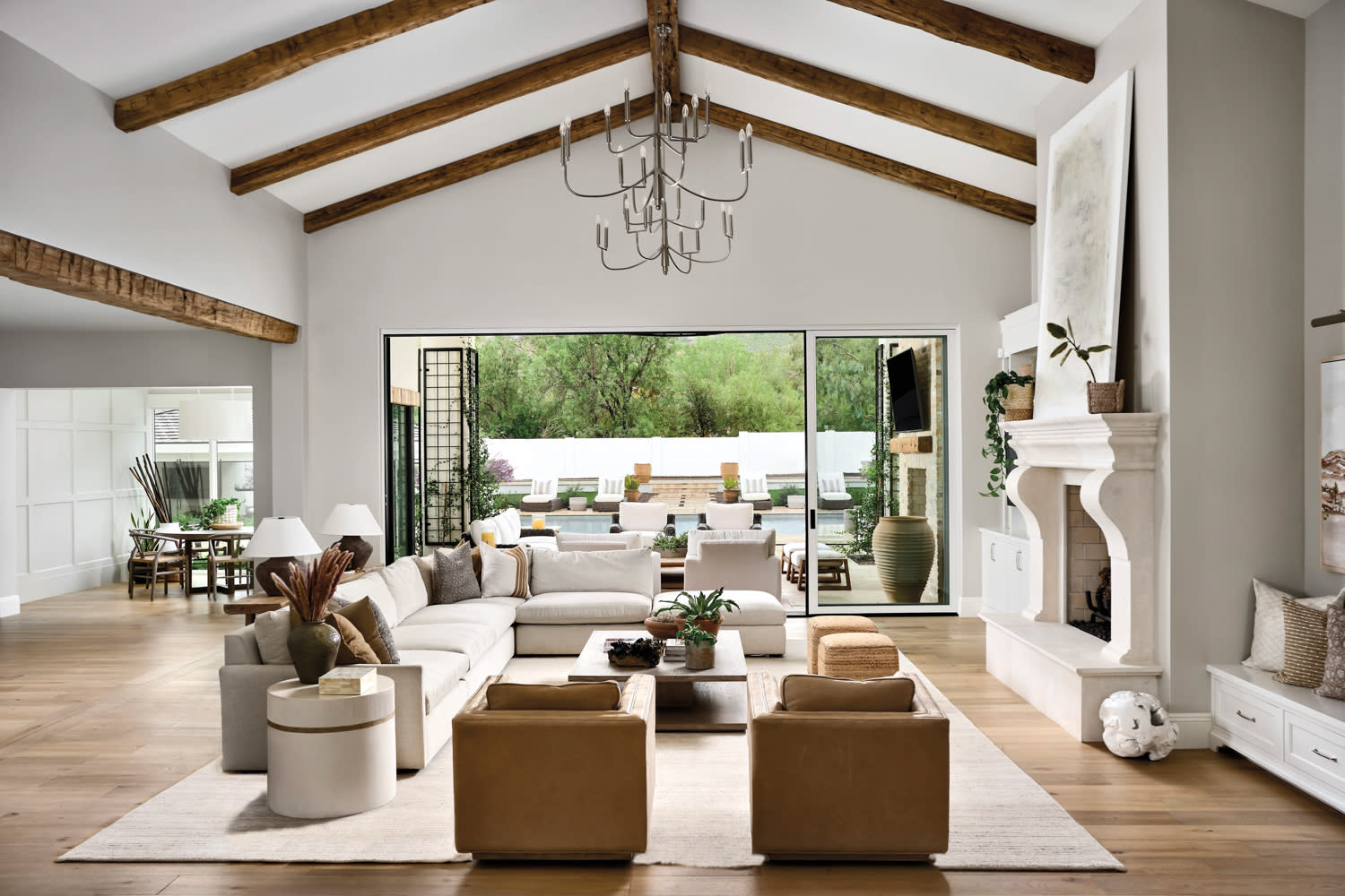 Living room with wood-beam ceilings, white sectionals, tan chairs and limestone fireplace by Lexi Lundberg