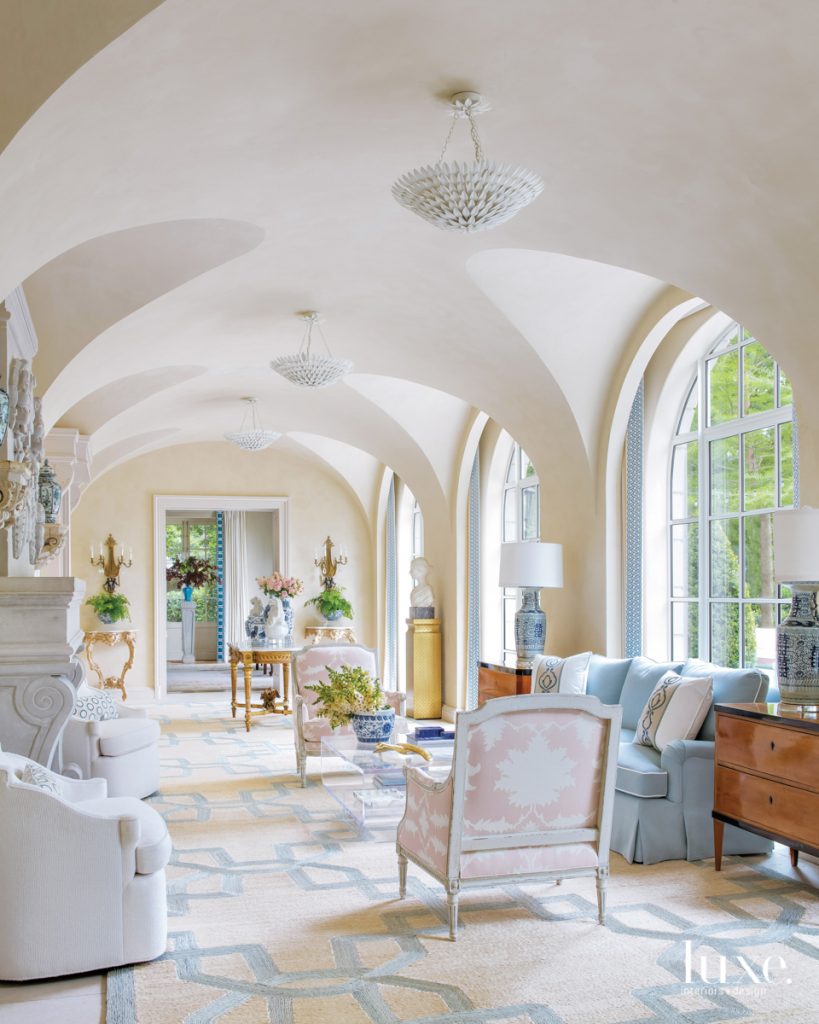 Olive Leaf dual-mount chandeliers from Shades of Light line the sun room ceiling. Louis XVI armchairs from Country French Interiors in Schumacher's blush-tone Garden of Persia fabric counter the blue-and-white palette: a lamp from Nick Brock Antiques, Mandeville draperies from Schumacher's Timothy Corrigan Collection and the sofa in Villa Nova's Atlantis Glacier material from Culp Associates.