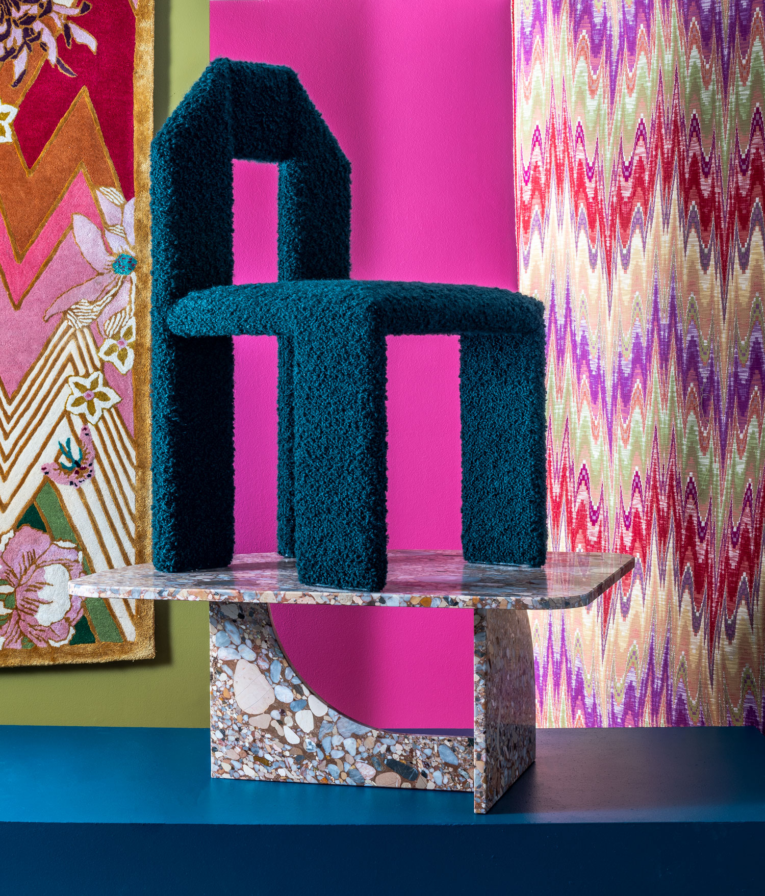 abstract blue chair on top of marbled table with pink drapes in background