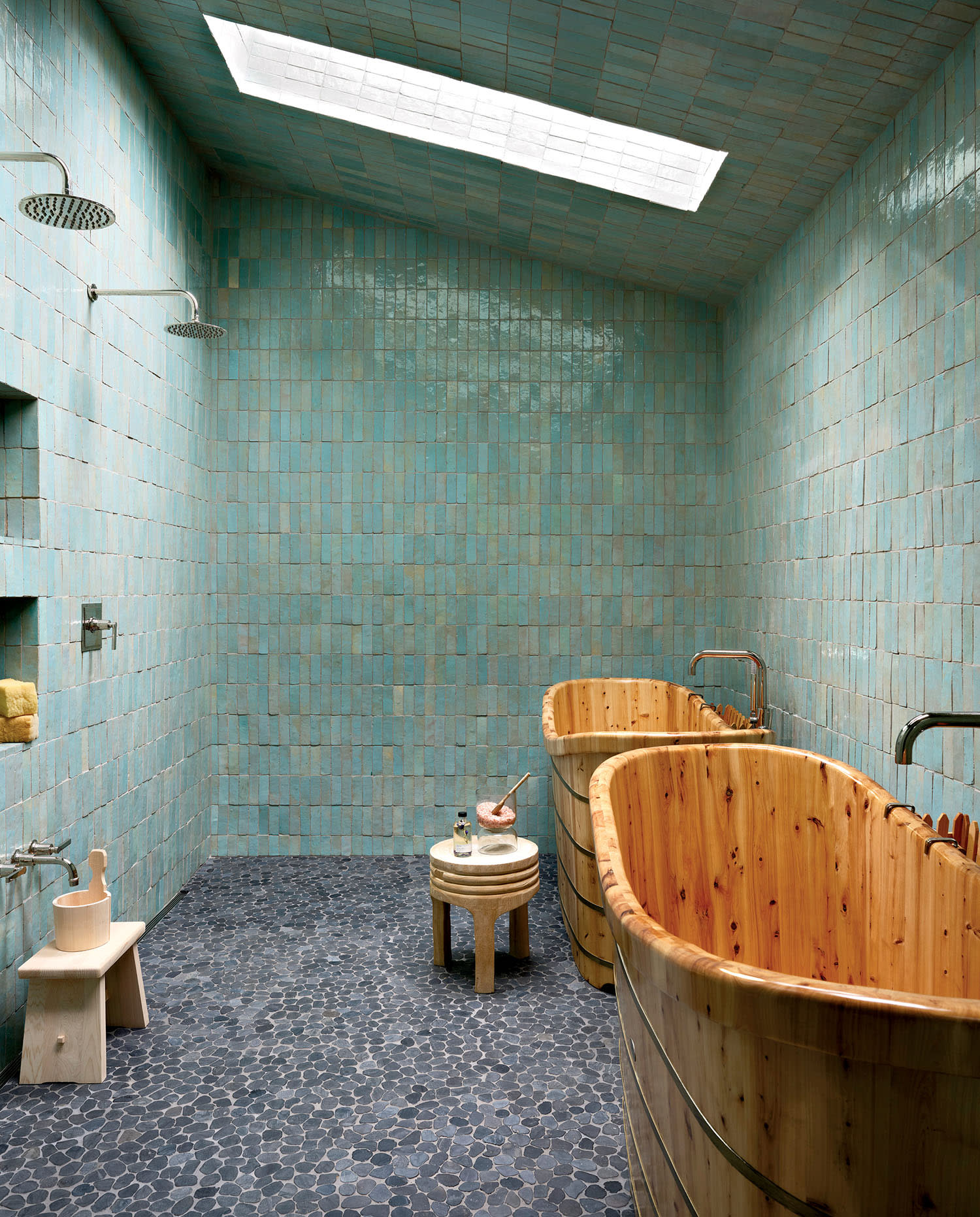 A sauna room with two shower heads, blue tiled walls, and two wooden bathtubs with matching faucets.