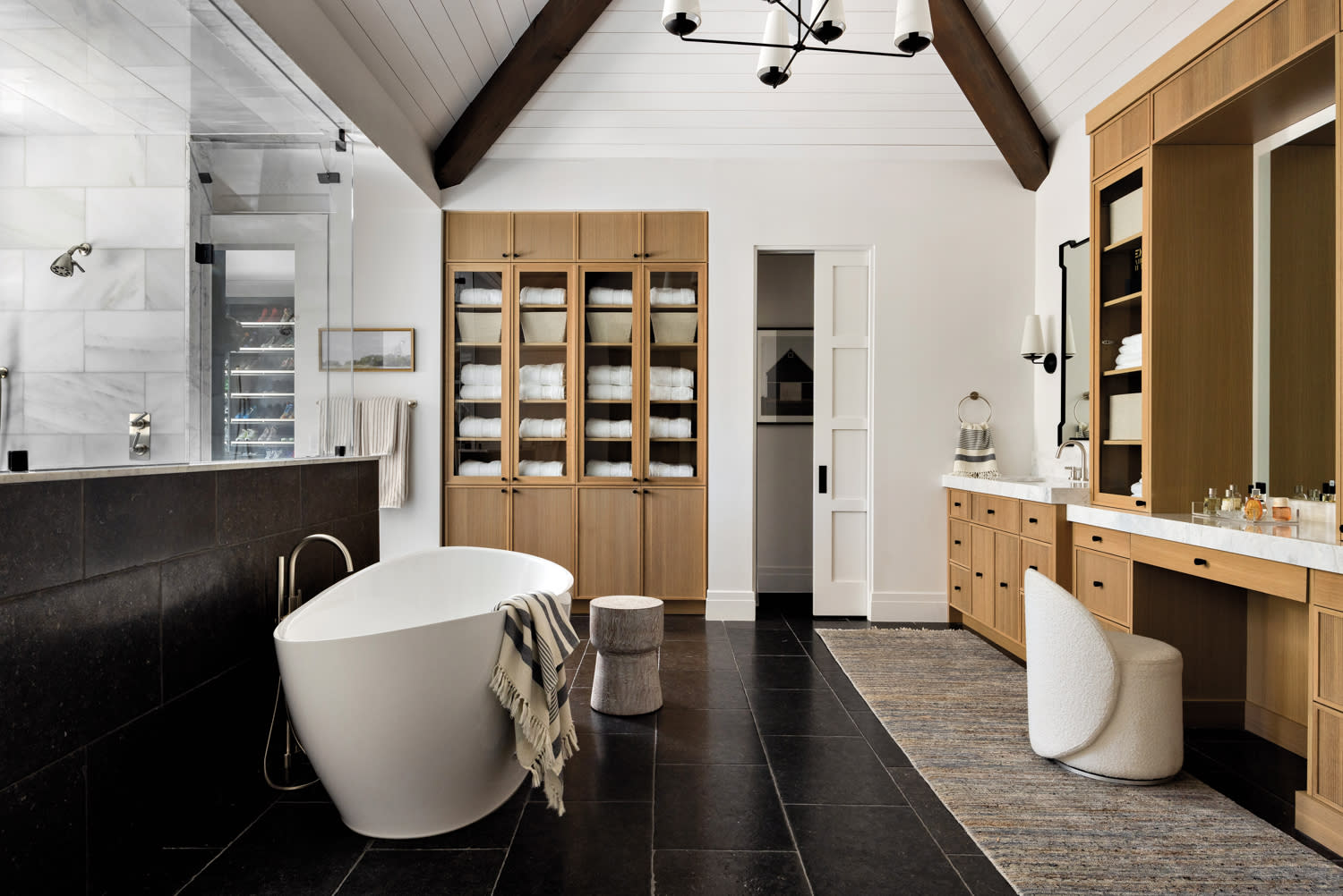 Spacious modern bathroom with black tile floor, freestanding tub with striped towel, wooden cabinets, and large vanity area. Cozy and elegant ambiance.