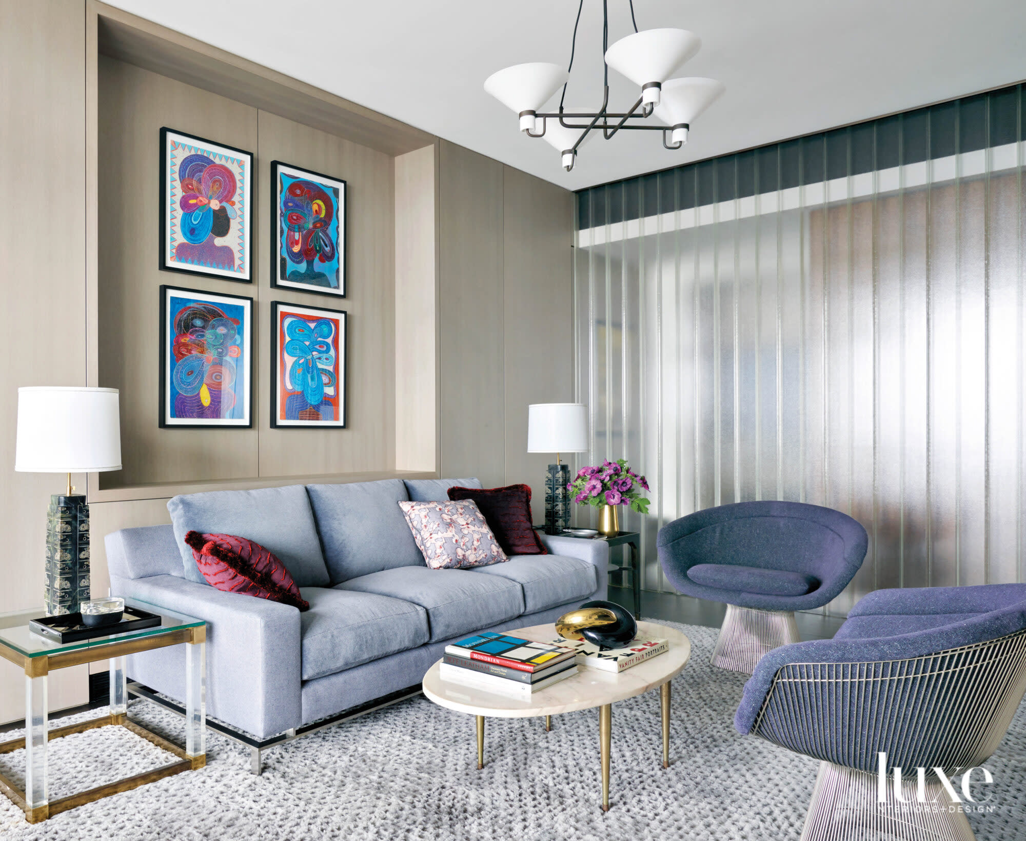 A blue sofa and blue midcentury chairs are set off by colorful paintings on the wall above the sofa.