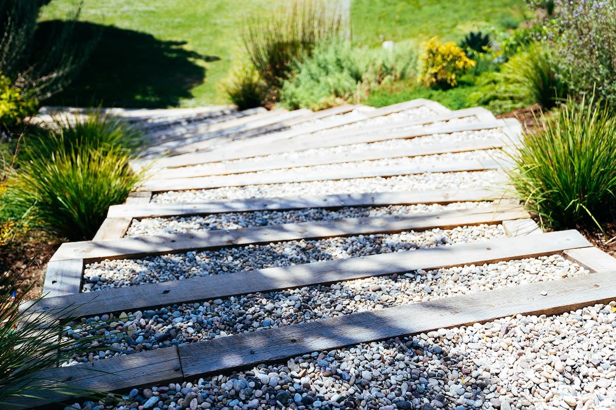 A wooden staircase set in gravel, flanked by lush plants, creating a serene outdoor pathway.