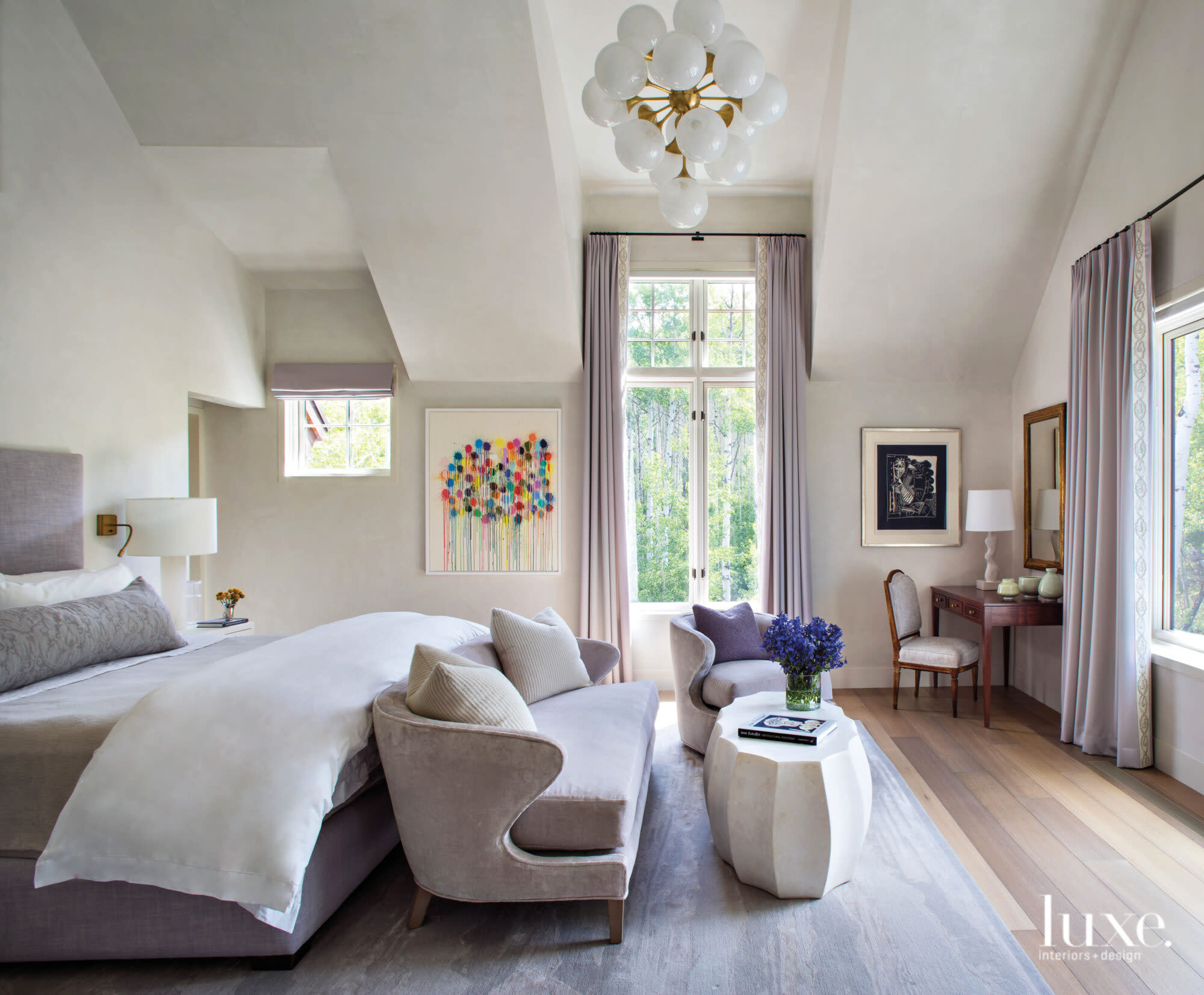 A light-filled bedroom has a small sofa at the foot of the bed.