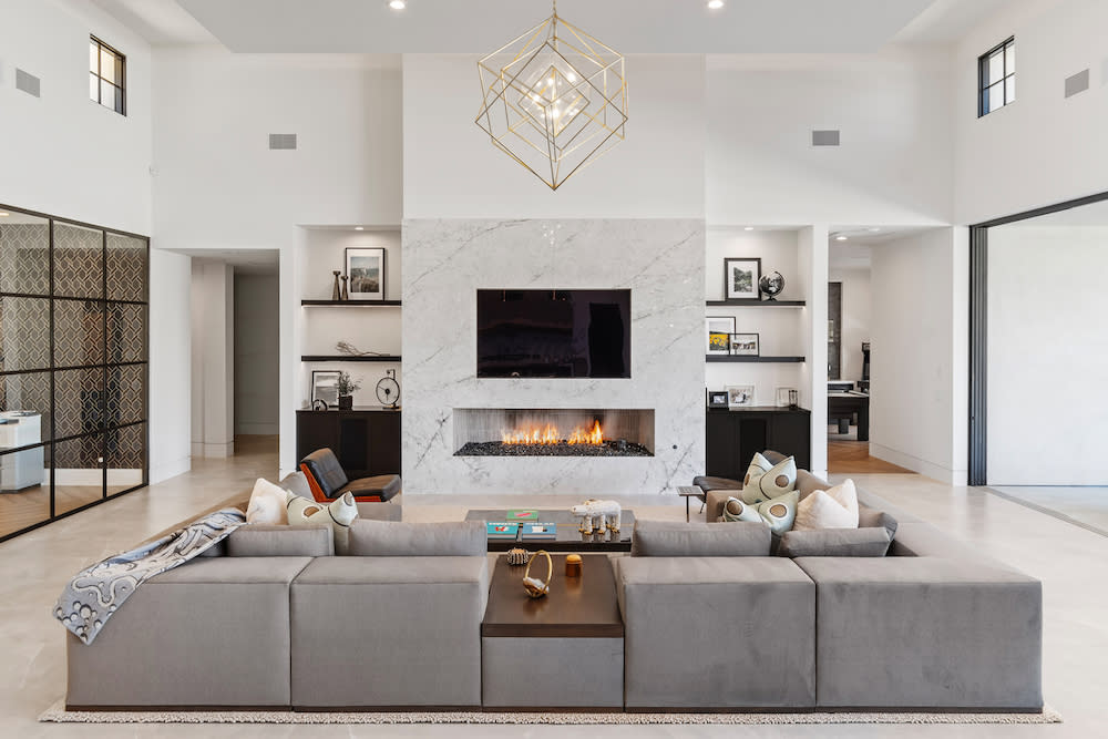 A contemporary living room with a fireplace, grey sectional couch and expansive windows.