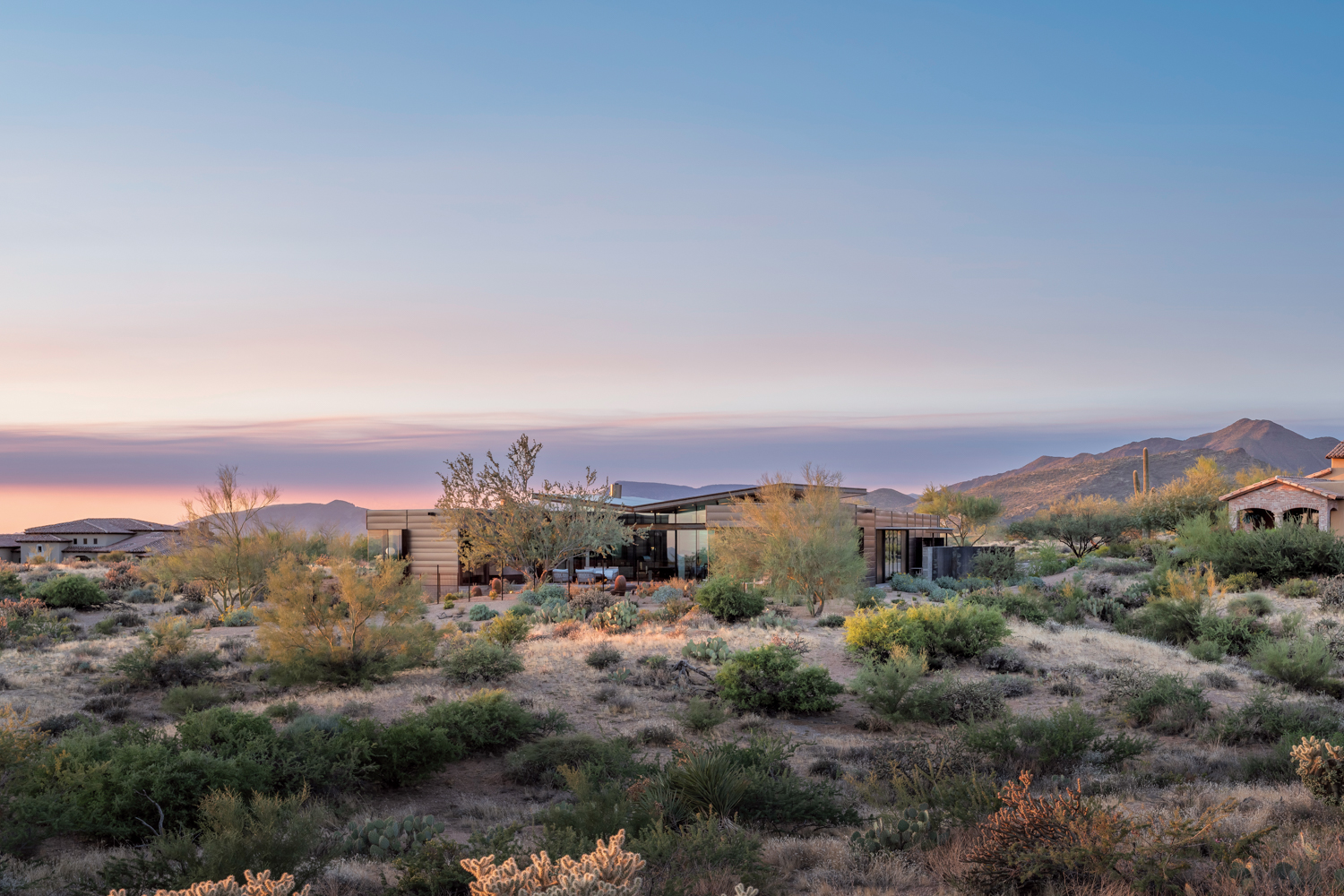 A one-story concrete-steel-and-glass house in the desert overlooking the mountains.