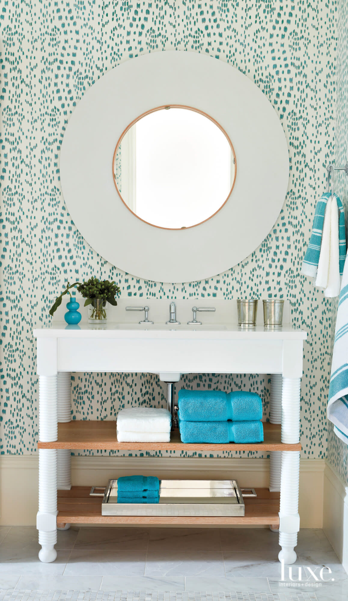 Guest bathroom with patterned wallcovering, round mirror and white vanity.