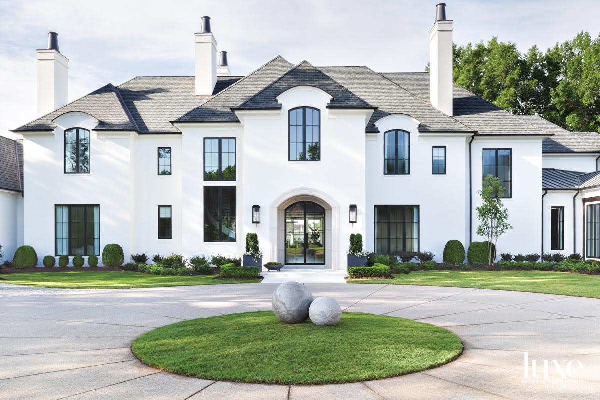 Large resident with white stucco exterior, gray roof and round portion of grass in the center of the motor court