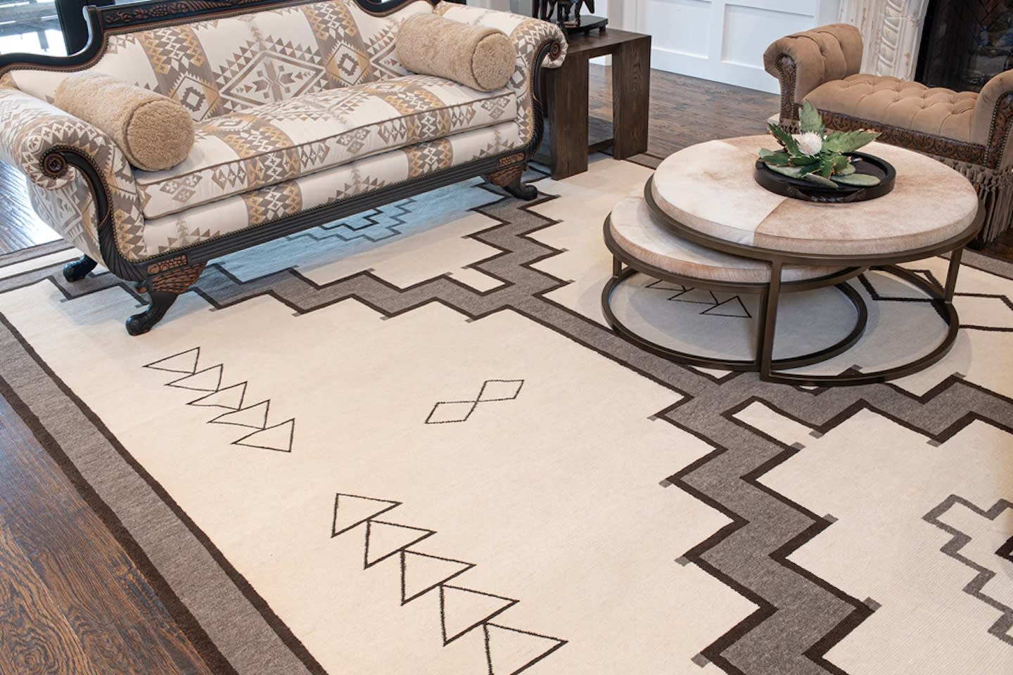 Elegant living room with a geometric beige and brown rug, patterned sofa, wooden table with rounded stone slabs, and a small plant centerpiece.