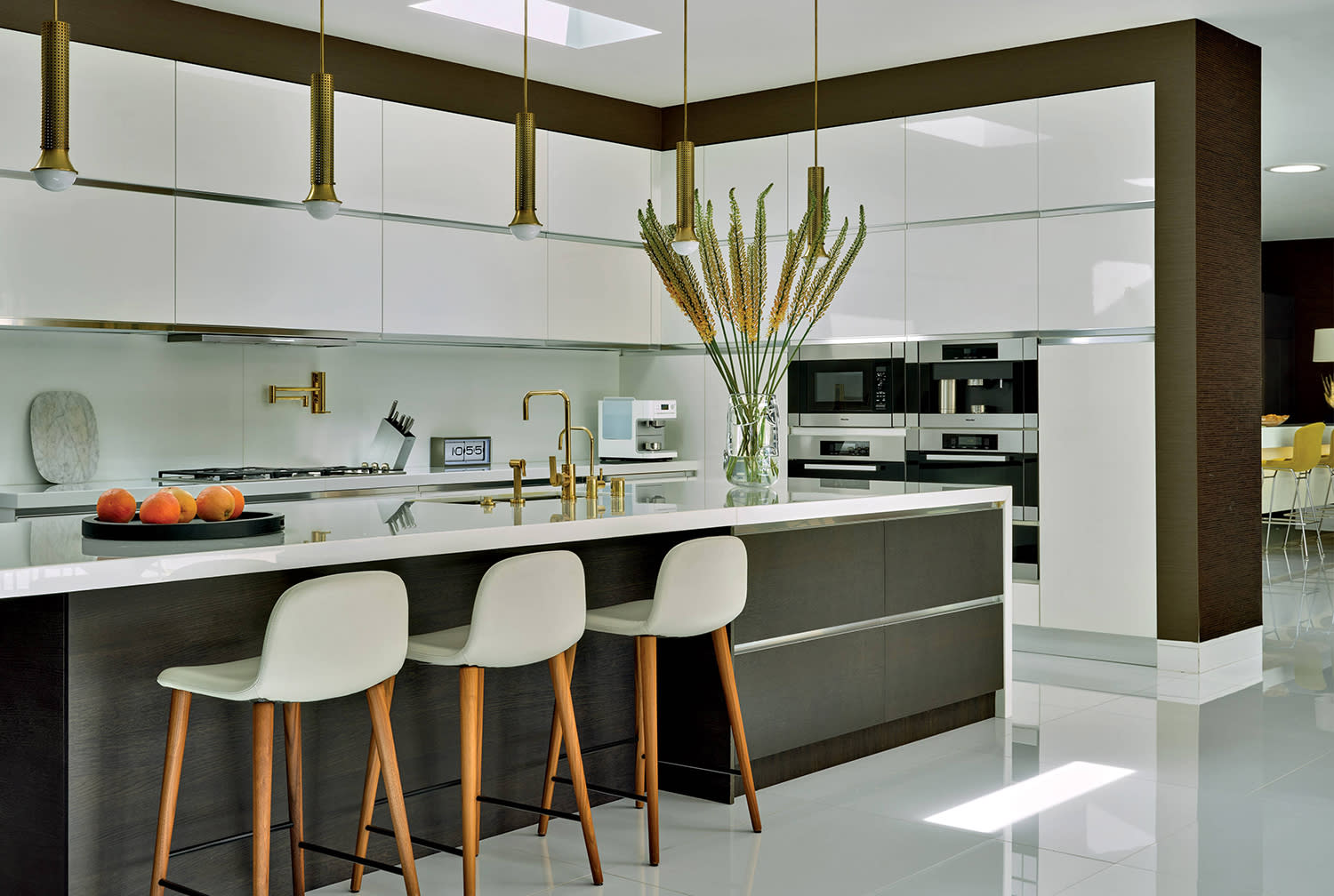 Three high-top upholstered chairs sit at an island in a kitchen with white cabinetry and wood accents. 