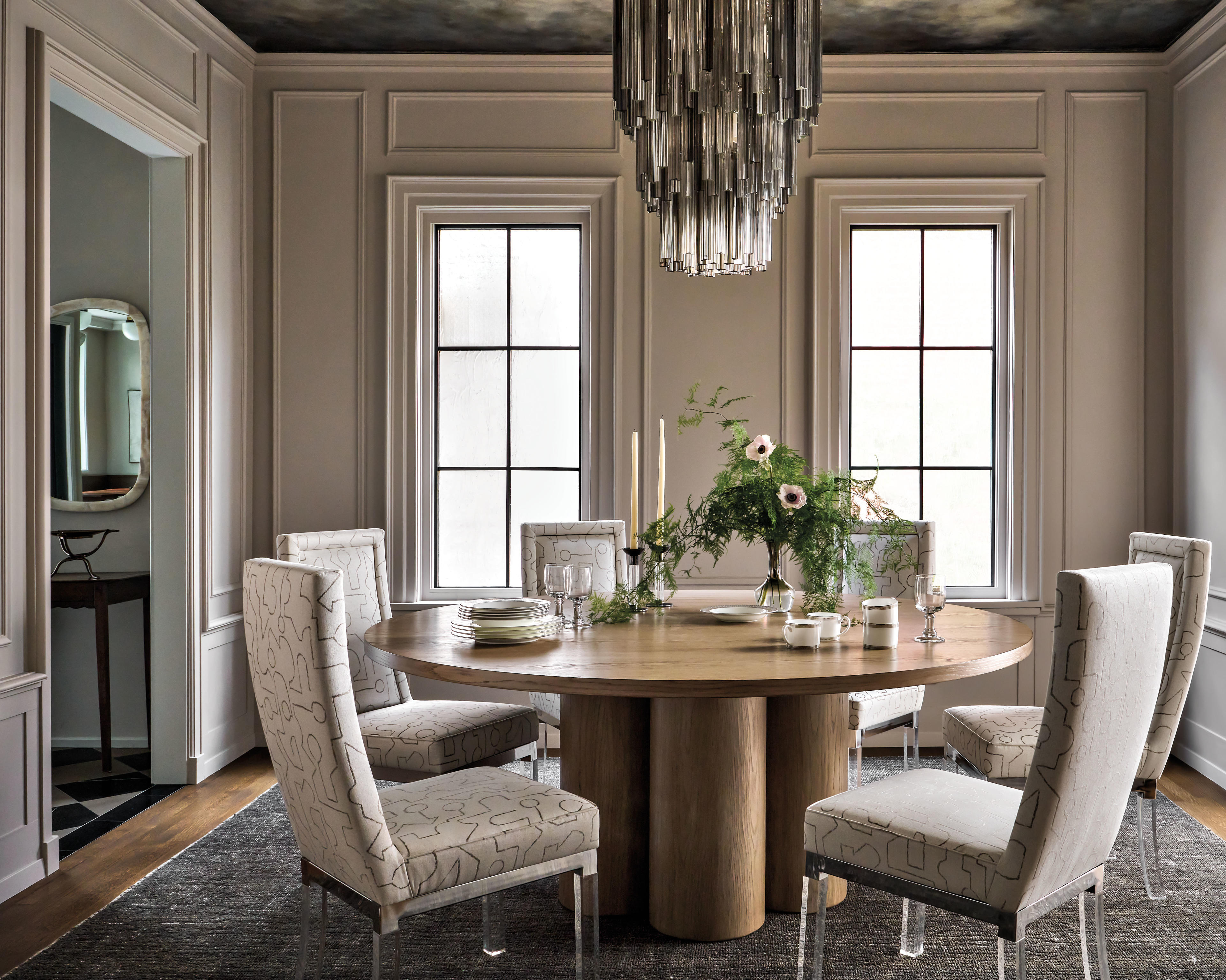 Murano-glass chandelier hangs above a circular dining table surrounded by chairs with graphic prints