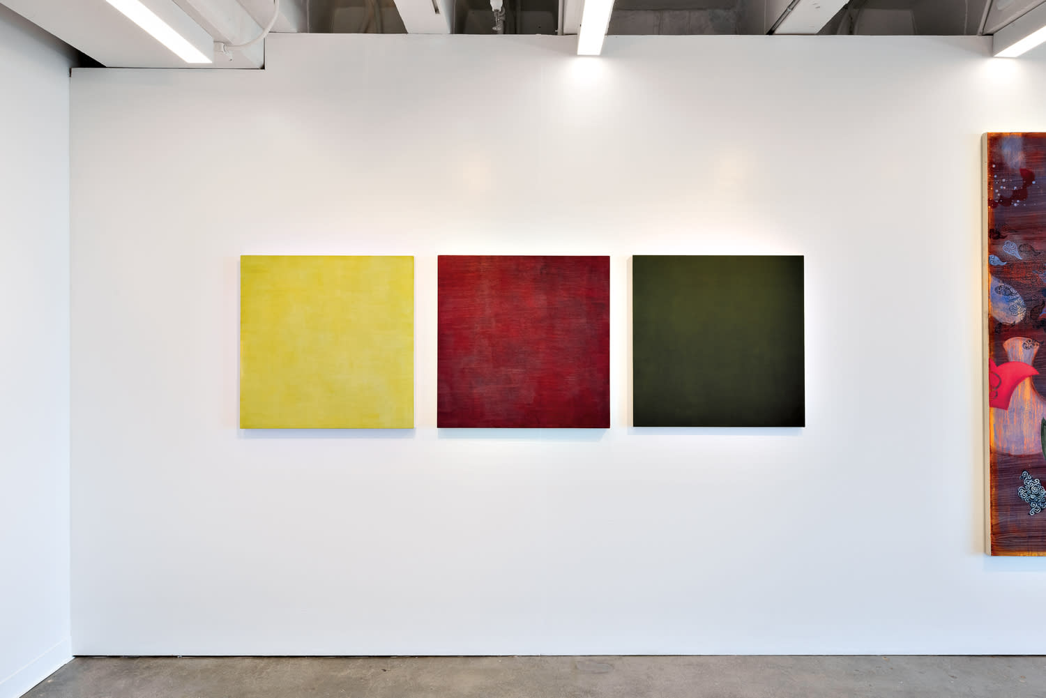 Three square artworks (one yellow, one red and one green) against a white wall.