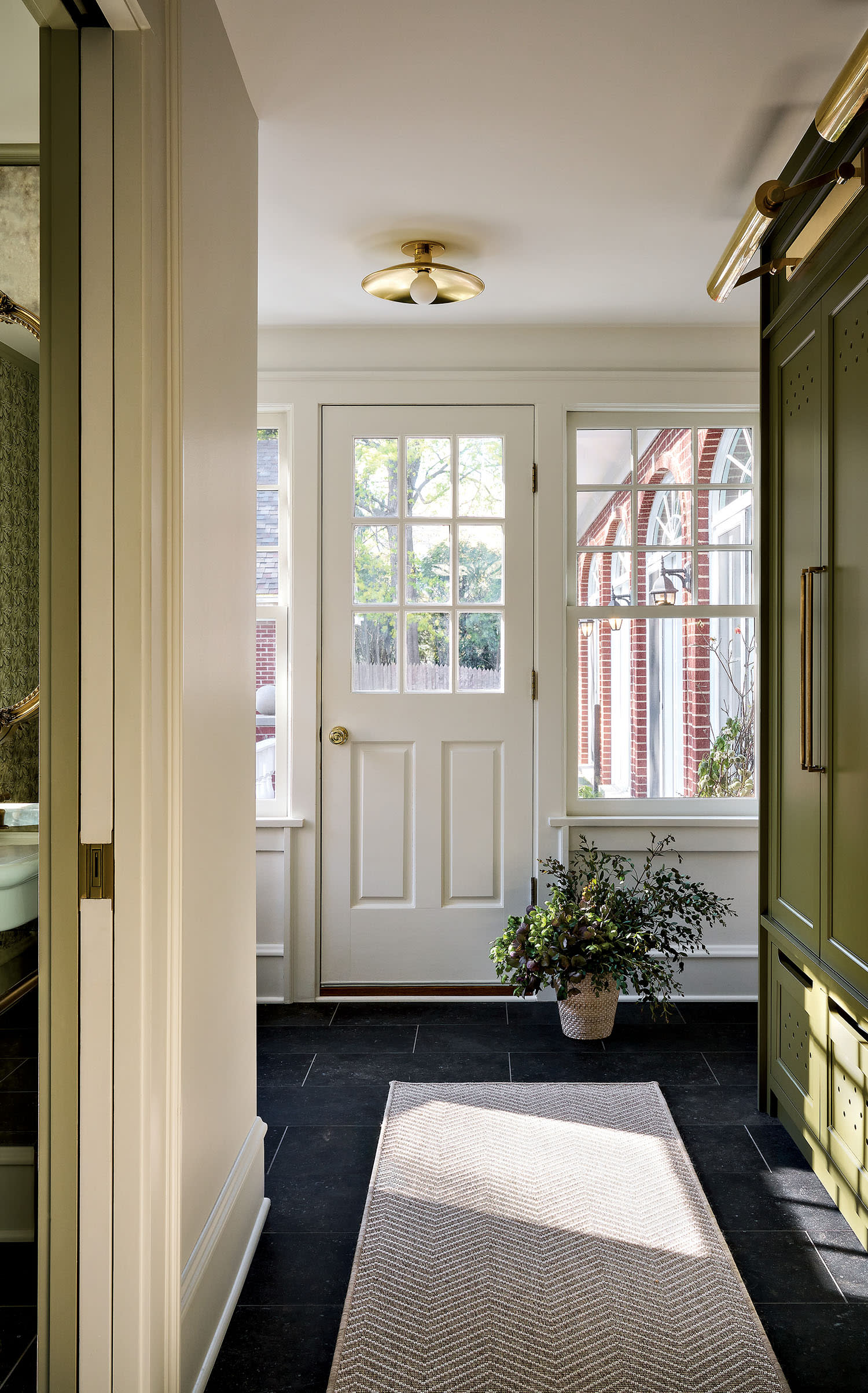 Mudroom with a white door and large windows letting in natural light, highlighting green cabinets and dark floor tiles