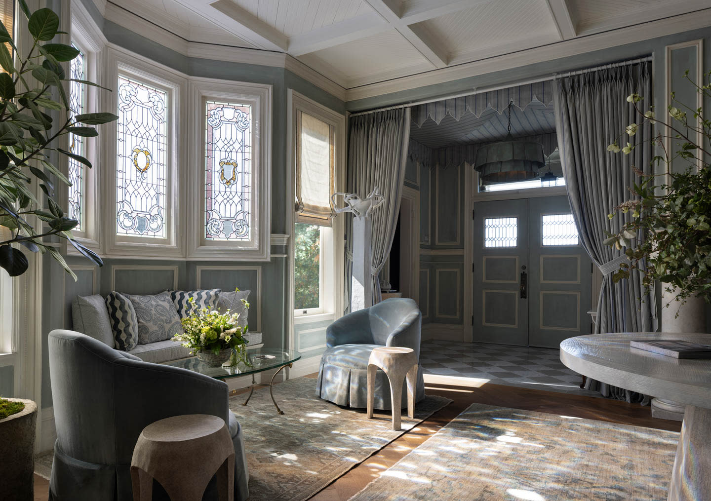 Elegant sitting room with light blue walls, stained glass windows, and classic decor. Features plush chairs, a loveseat, and a glass coffee table.