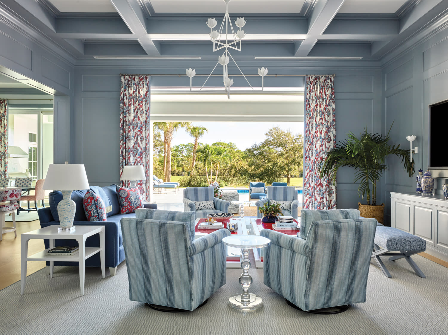 living room by Jackie Armour with blue walls, striped armchairs, patterned draperies and red accents