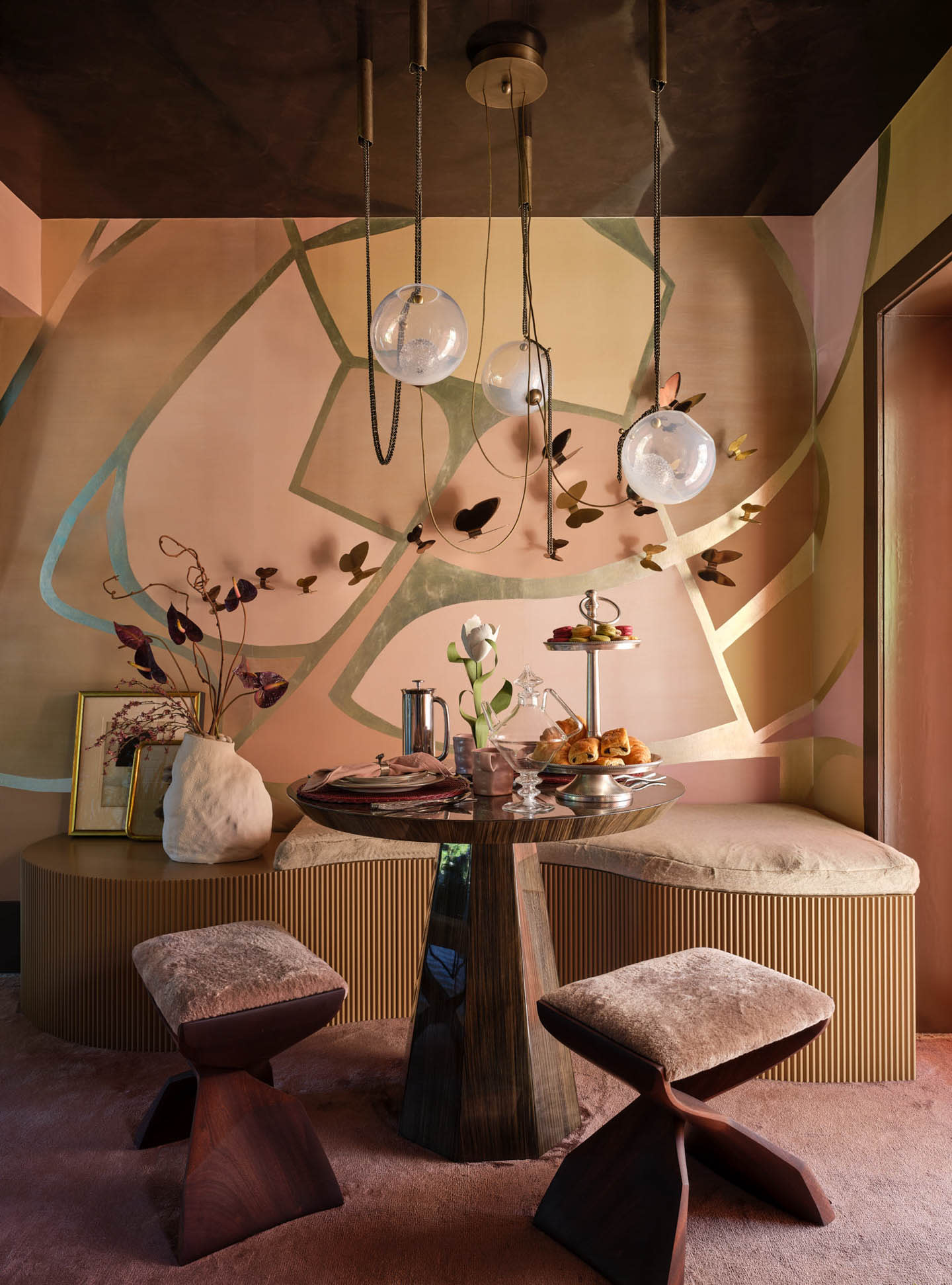 Cozy dining nook with a round table and plush stools. Abstract wall art, modern pendant lights, and a vase with flowers create a warm, artistic ambiance.