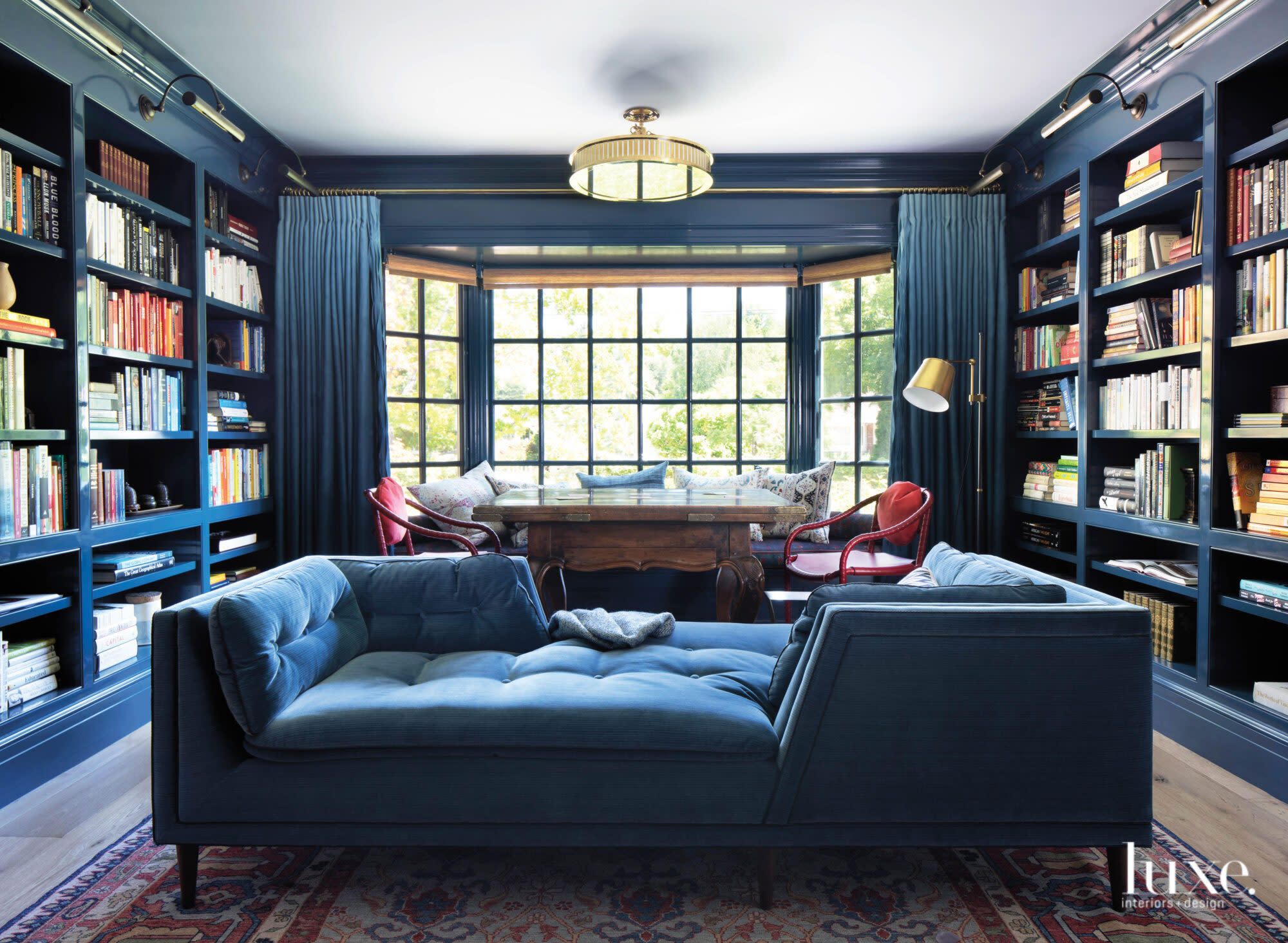 In the library, a two-sided sofa and a game table make the dark blue room multifunctional.