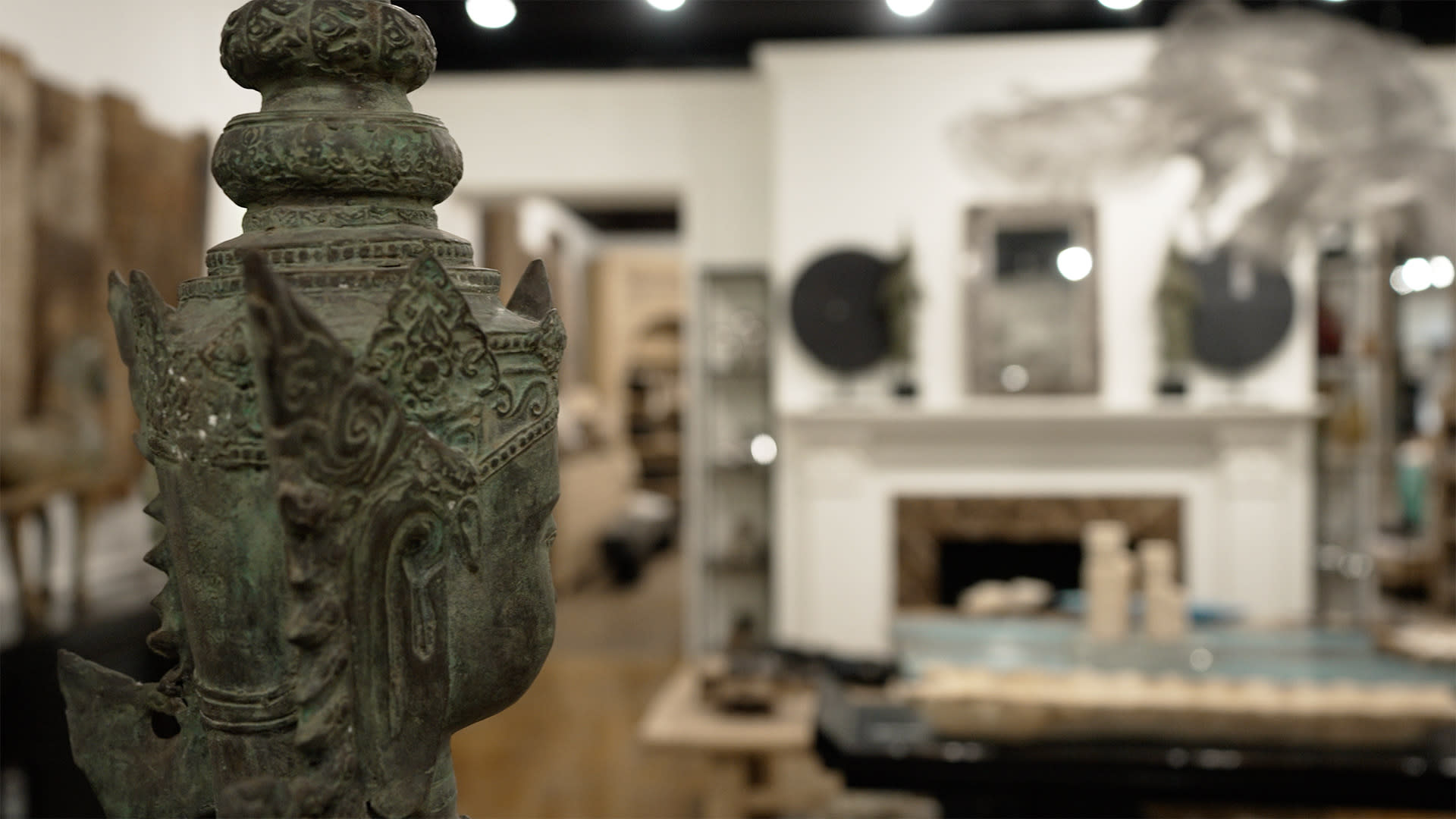 ornate, green bronze statue of a deity with intricate patterns, set in a room with eclectic decor