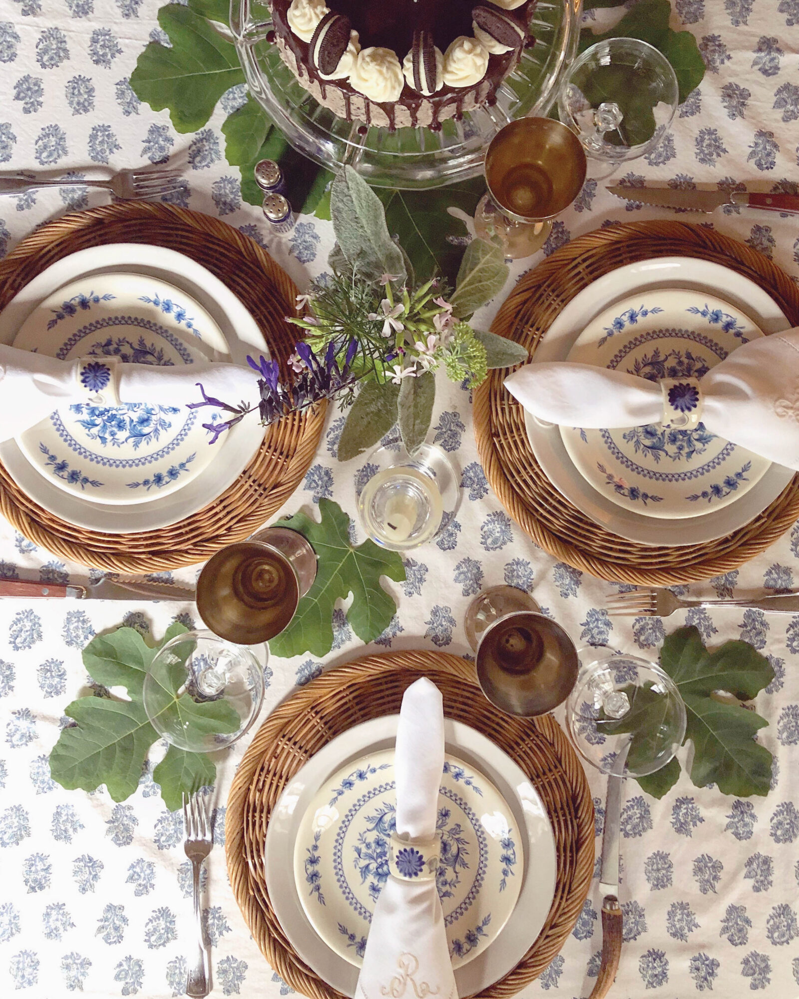 table setting of printed linens and wicker chargers with surrounding greenery