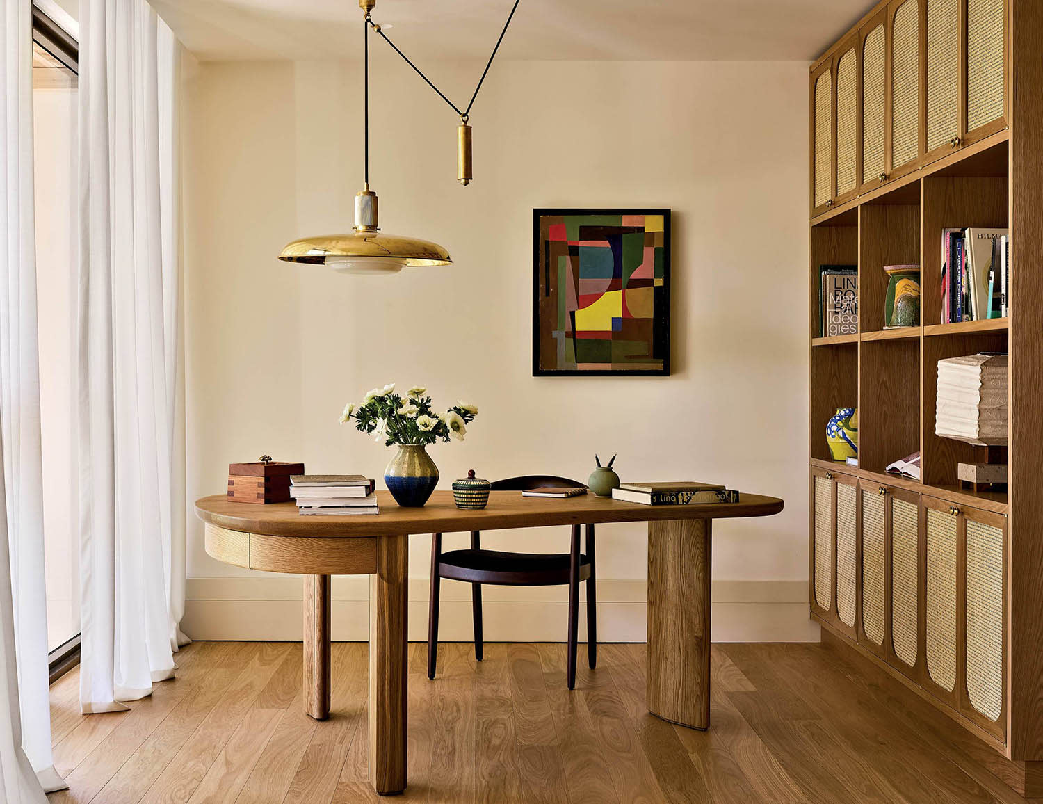An office with a wooden desk and chair sitting under an overhead light and next to nearby shelving.