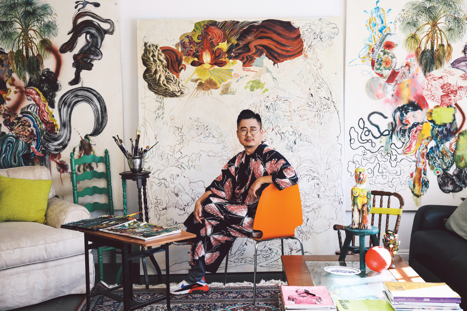Artist Ken Gun Min in his studio, sitting in from of an unfinished canvas.