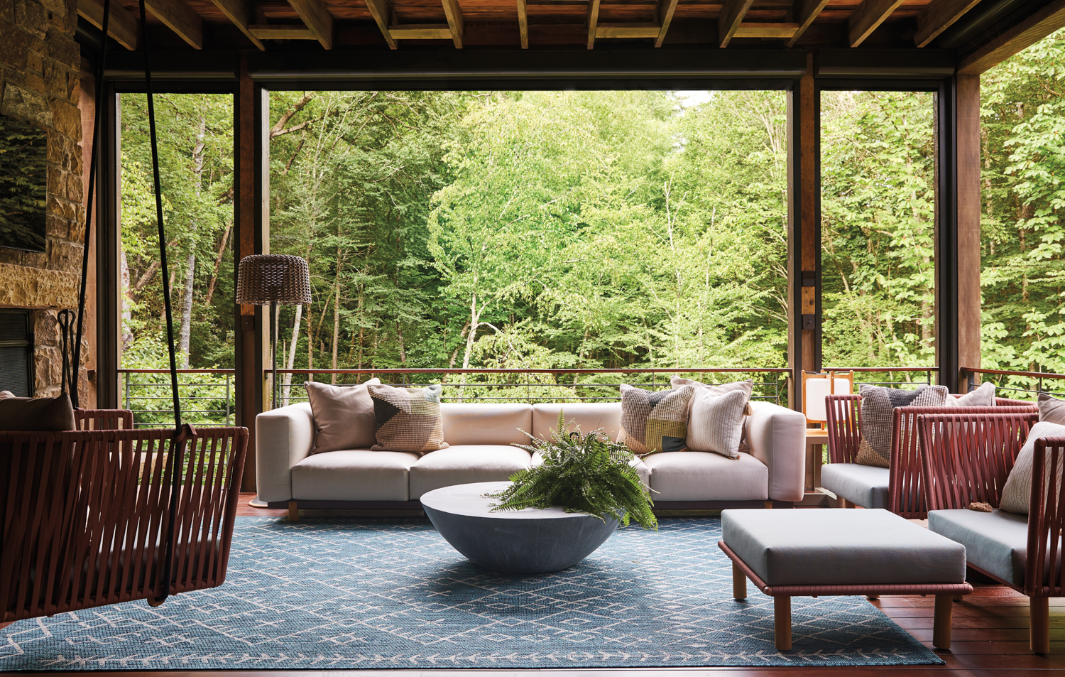 A rustic porch furnished with modern outdoor seating—and surrounded by greenery by Teri Thomas