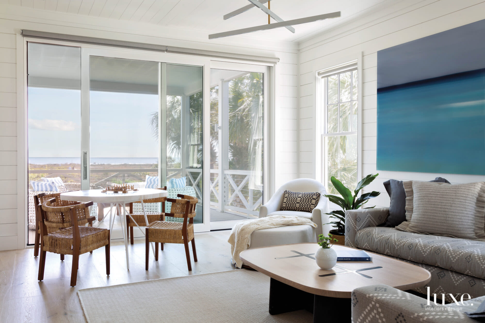 Family room overlooking the ocean featuring upholstered seating, oval coffee table, game table with chairs and sliding screen doors to a porch