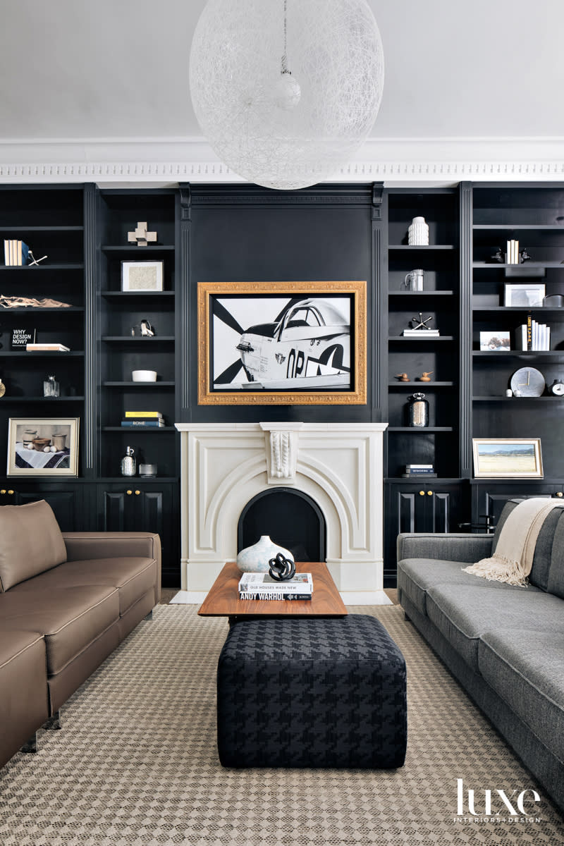 A living room with black walls and bookshelves. An airplane photograph hangs above a white mantle.