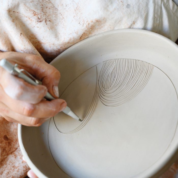 Artist Linda Fahey carves a woodblock-like pattern into a serving plate.